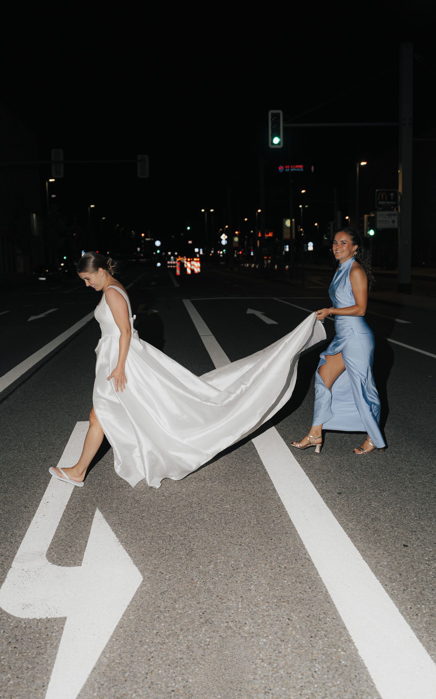 Wedding party posing on street at night with flowing white dress against road markings.