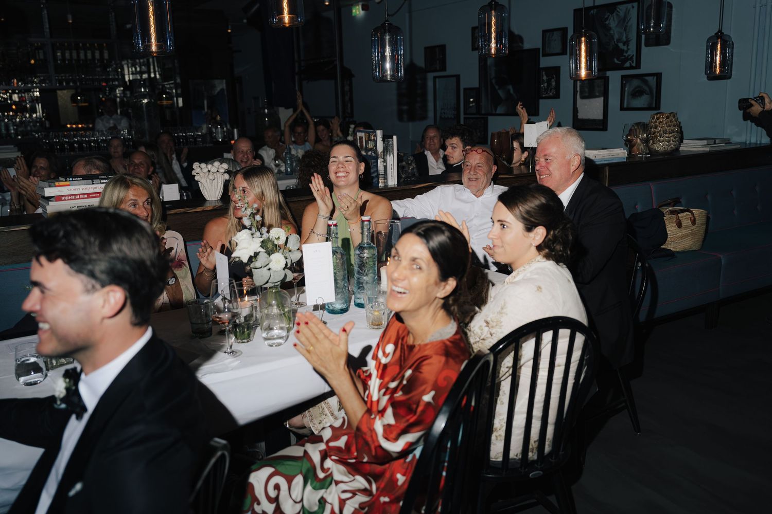 Wedding reception dining room with guests seated at long tables under warm lighting.