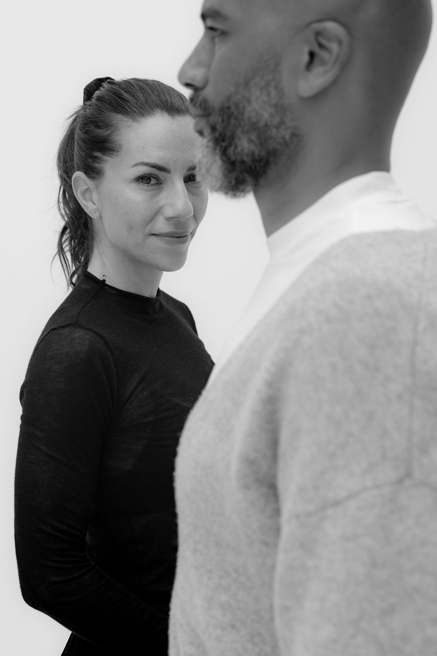 Black and white portrait of a woman in black top and a bearded man in light sweater facing each other.