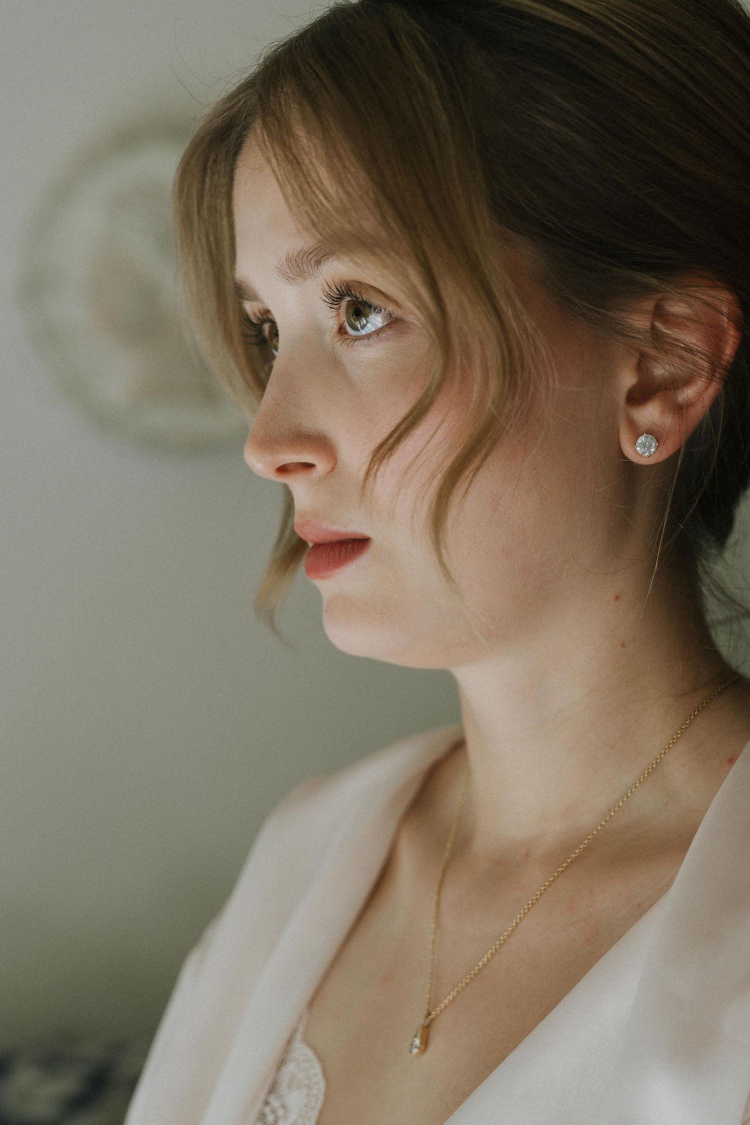 Close-up portrait of a young woman wearing diamond stud earrings and a delicate gold pendant necklace.