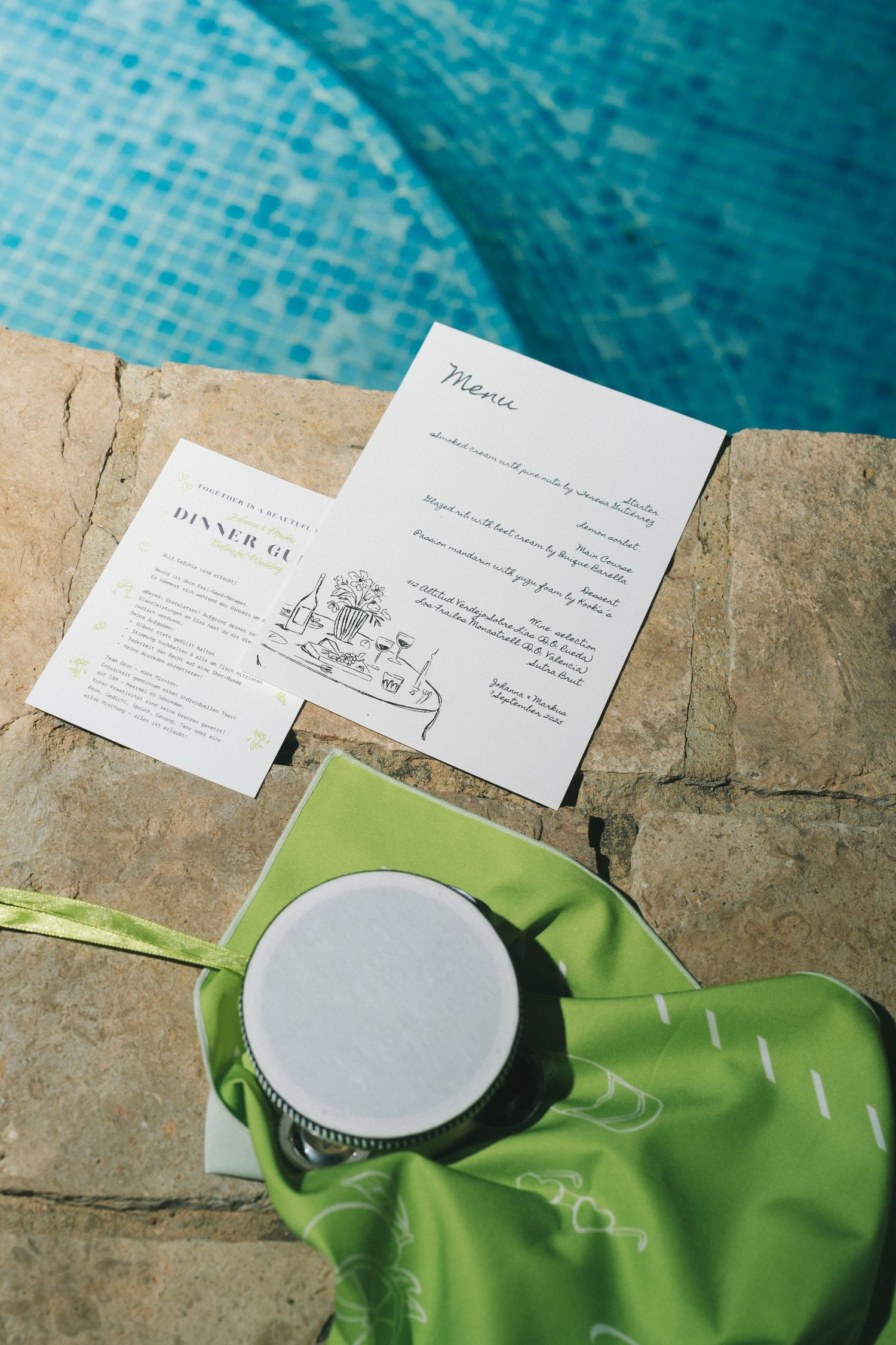 Wedding invitation cards and stationery displayed on green fabric by a pool edge.