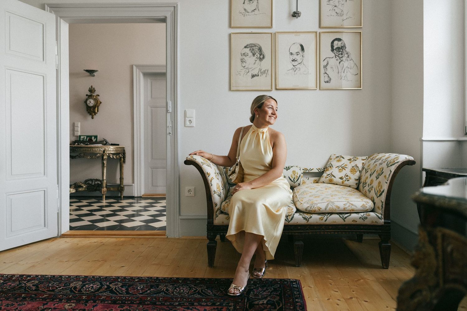 Interior scene with yellow dress, vintage furniture, and framed sketches on wall.