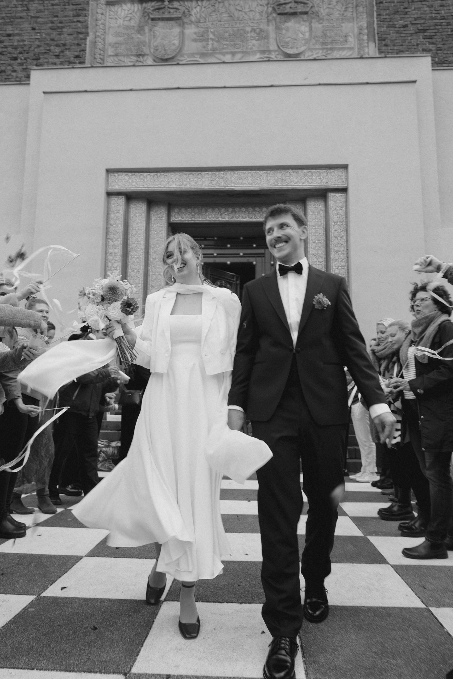 A joyful wedding exit with guests throwing confetti on a checkered walkway.