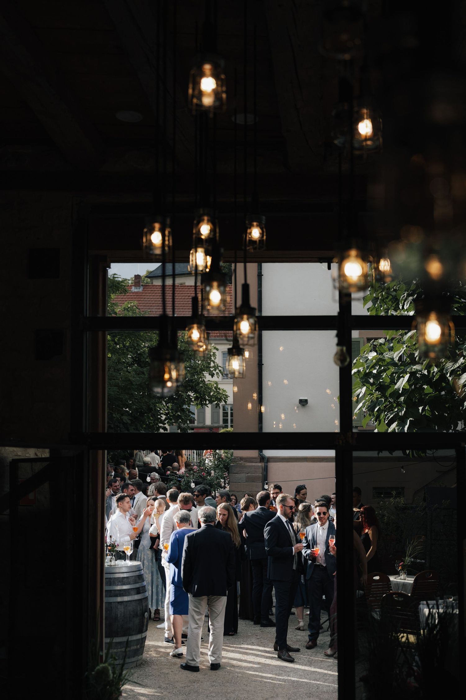 Hanging vintage light bulbs frame a view of wedding guests through a dark doorway.