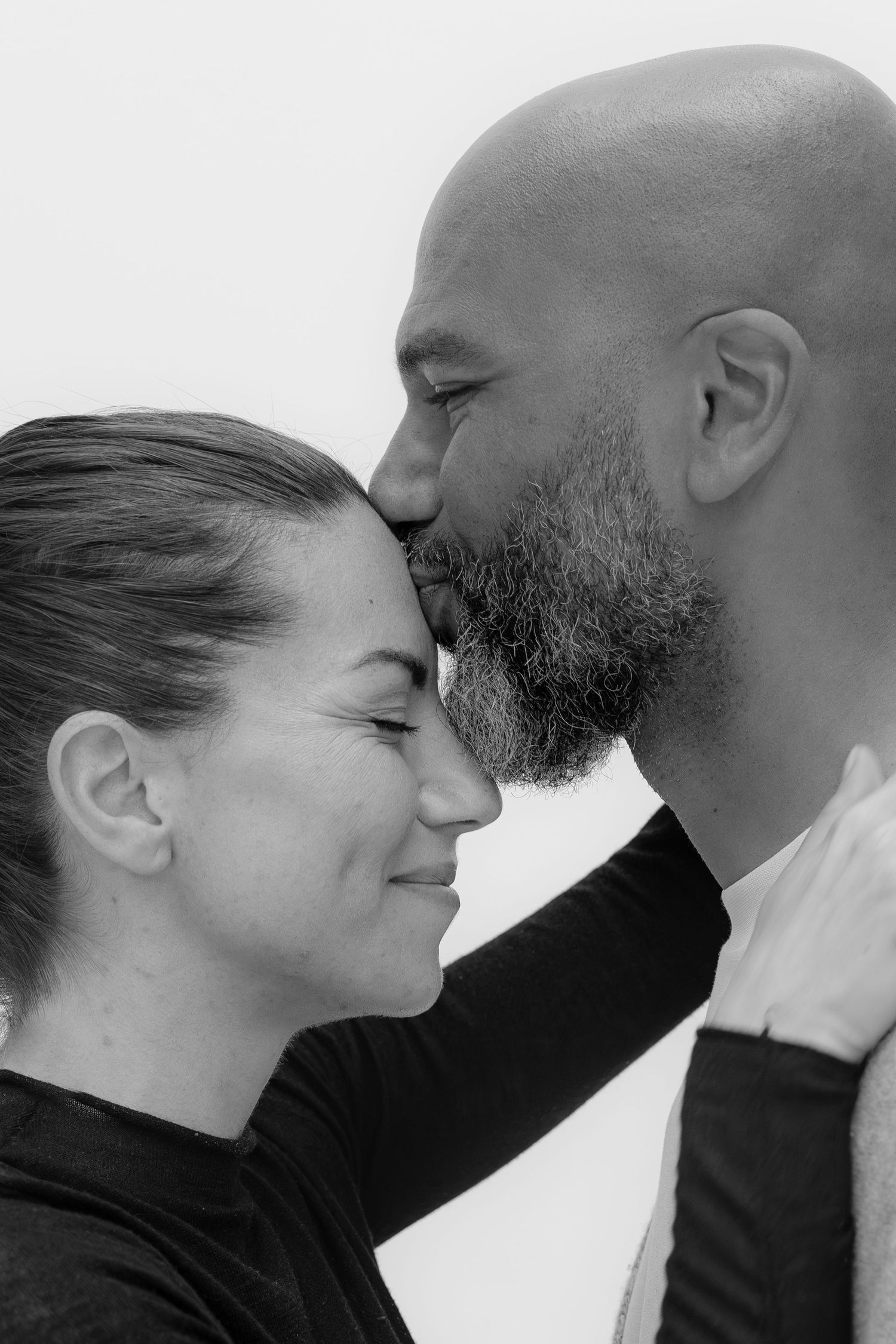Black and white photo of a couple sharing a tender moment, man kissing womans forehead while she smiles softly.