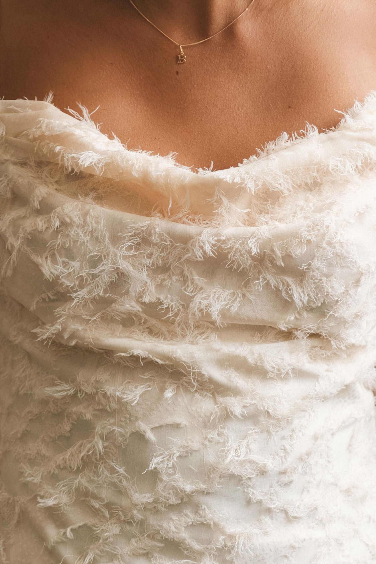 Close-up of delicate feathered texture on white wedding dress bodice with thin necklace.