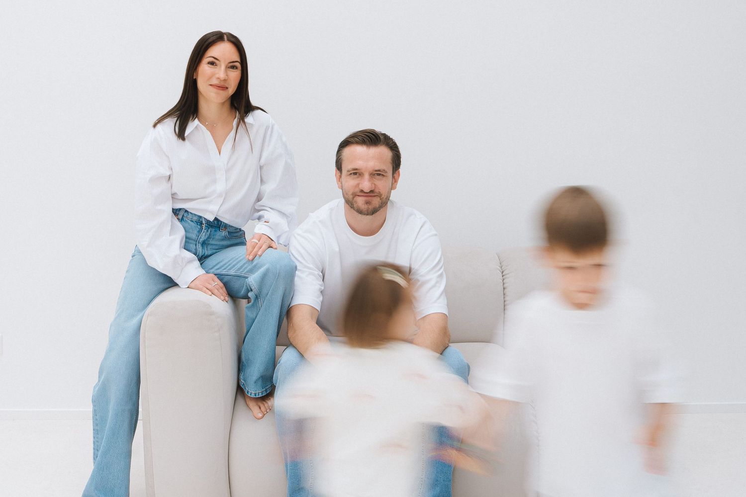 Happy family with two young children, parents sitting on a couch smiling in a bright white modern living room.