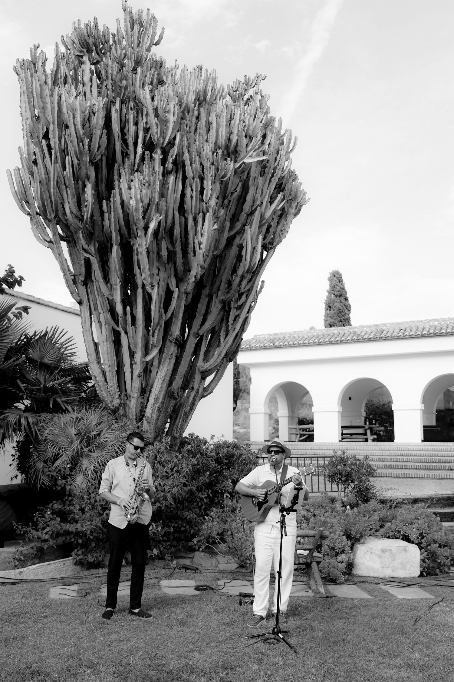 People posing by large cactus plants in front of Spanish colonial style building.