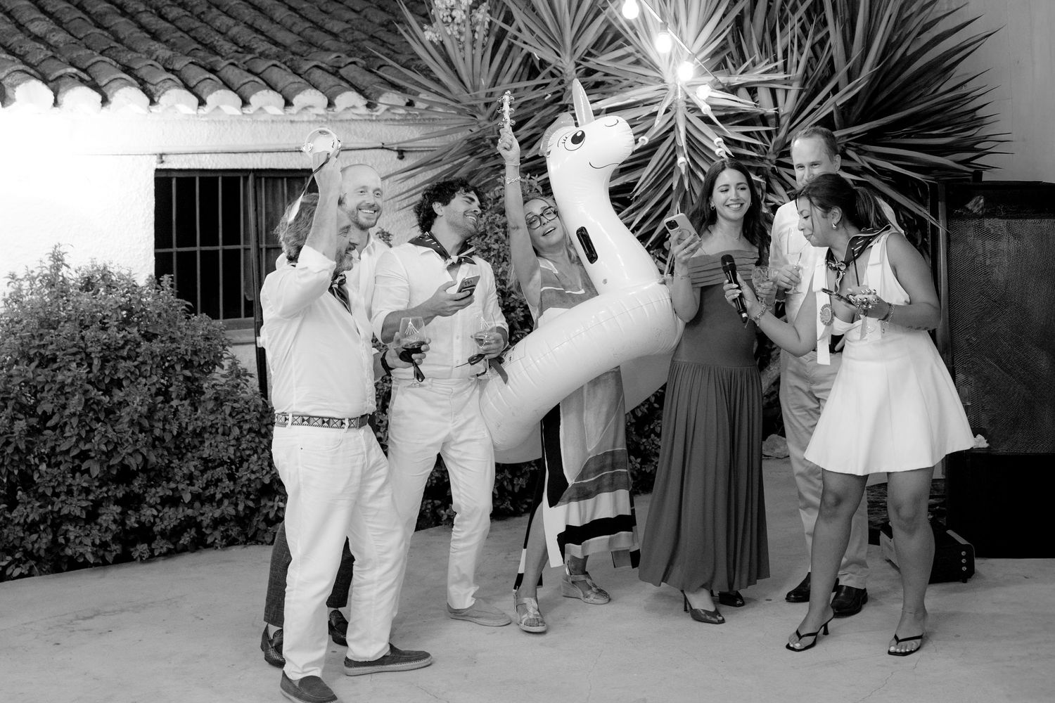 Black and white photo of wedding guests dancing in a line formation outdoors.