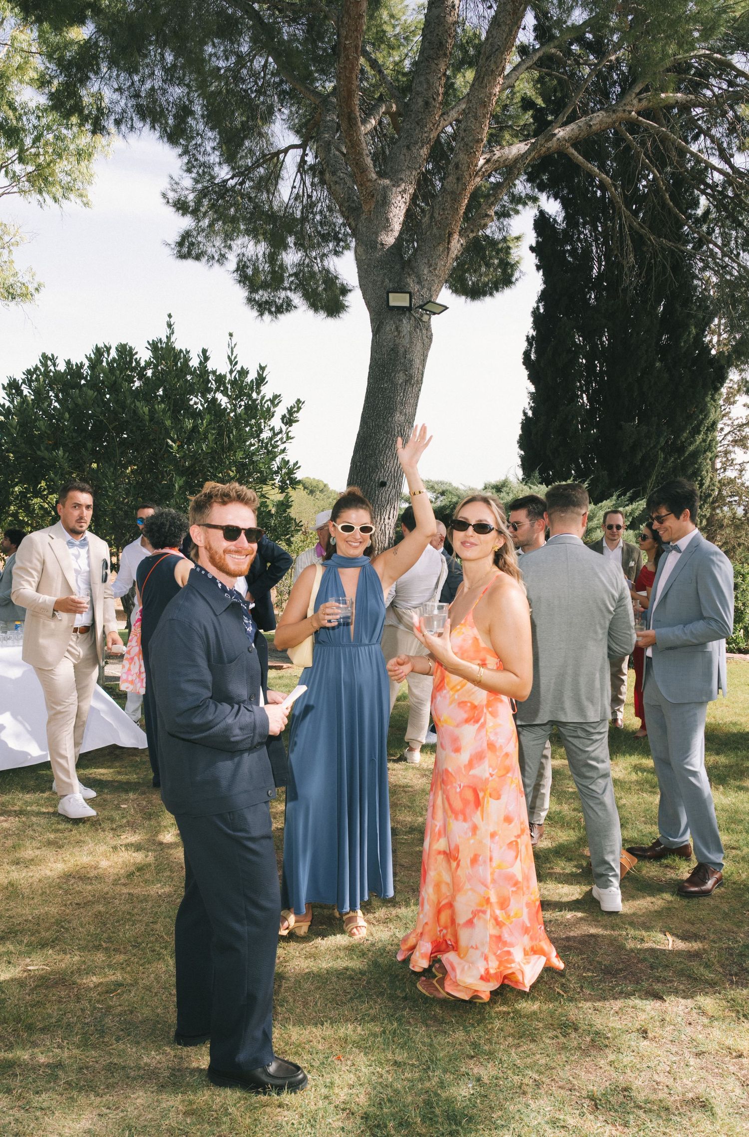 Wedding guests socializing on a grassy lawn with trees in the background.