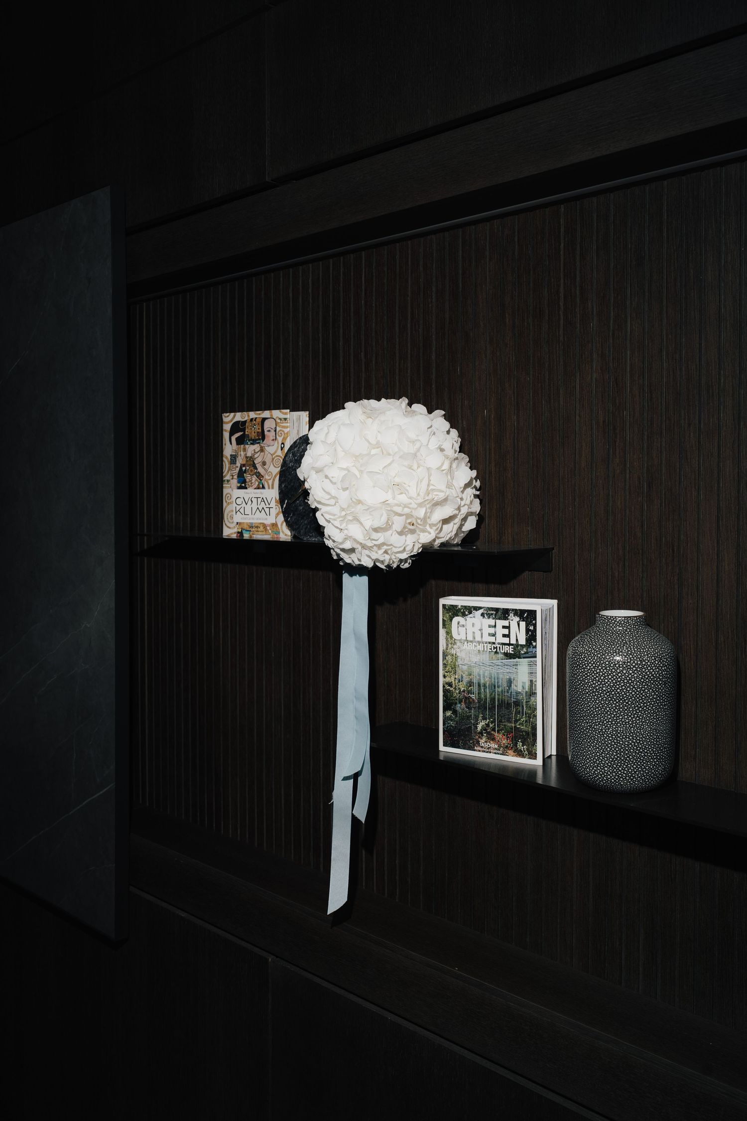 Dark wall shelf displaying decorative items and white floral arrangement with blue accent.