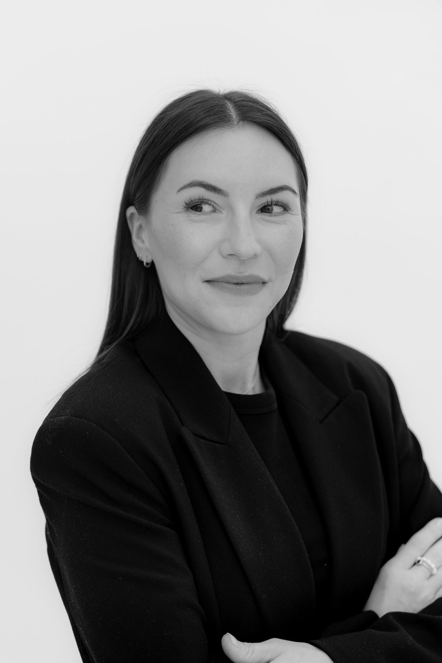 Black and white professional headshot of a woman in a blazer with arms crossed, smiling confidently.