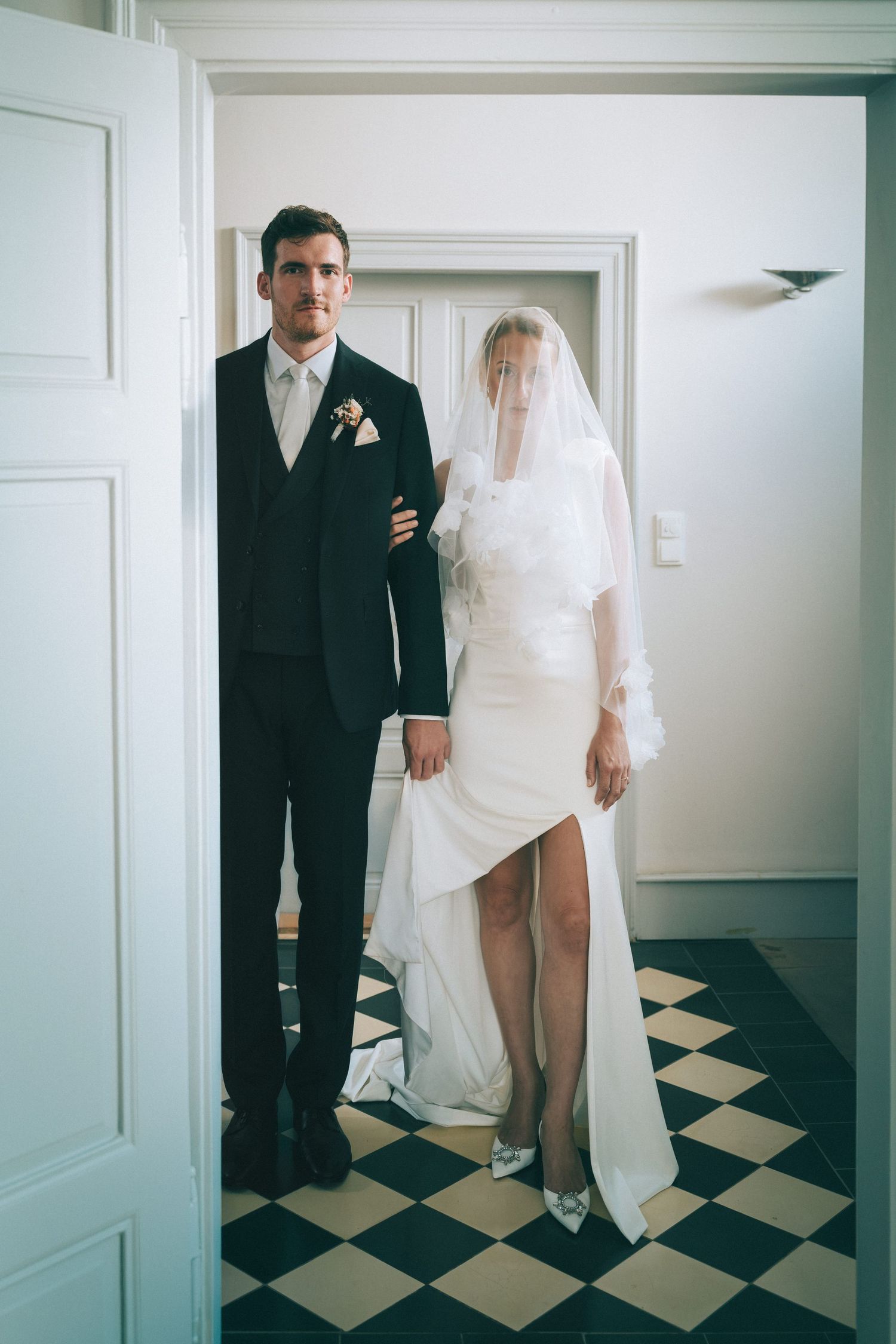 Wedding couple poses on black and white checkered floor in intimate indoor setting.