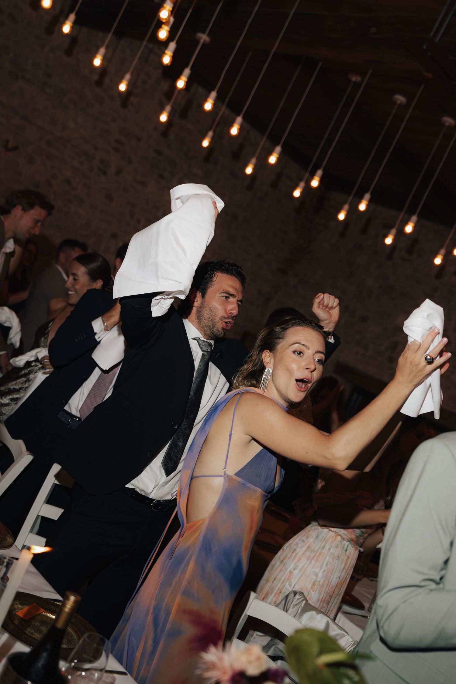 Party guests dancing enthusiastically under pendant lighting at an evening celebration.