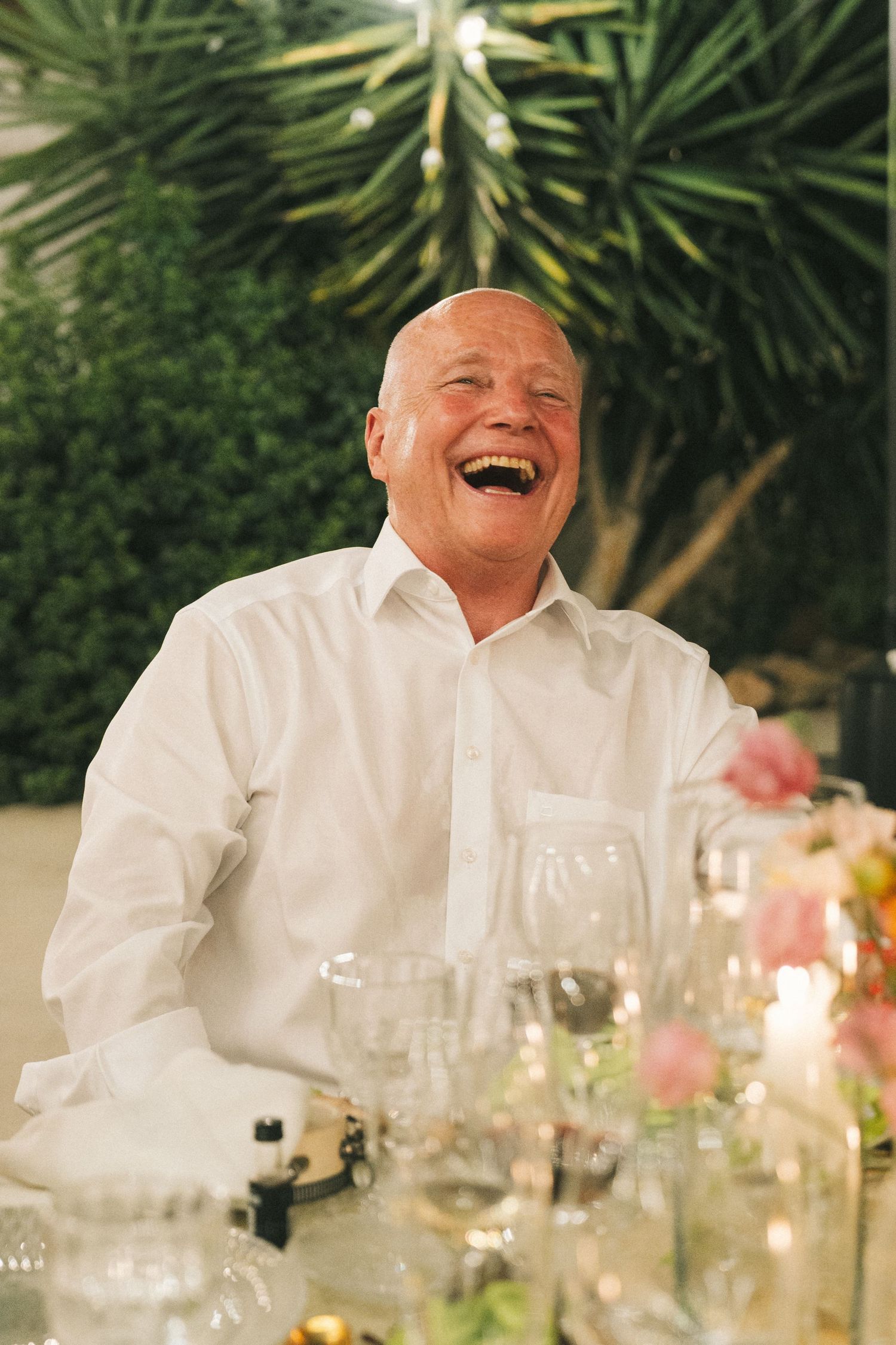 Guest enjoying dinner conversation at an outdoor evening reception with palm trees in background.