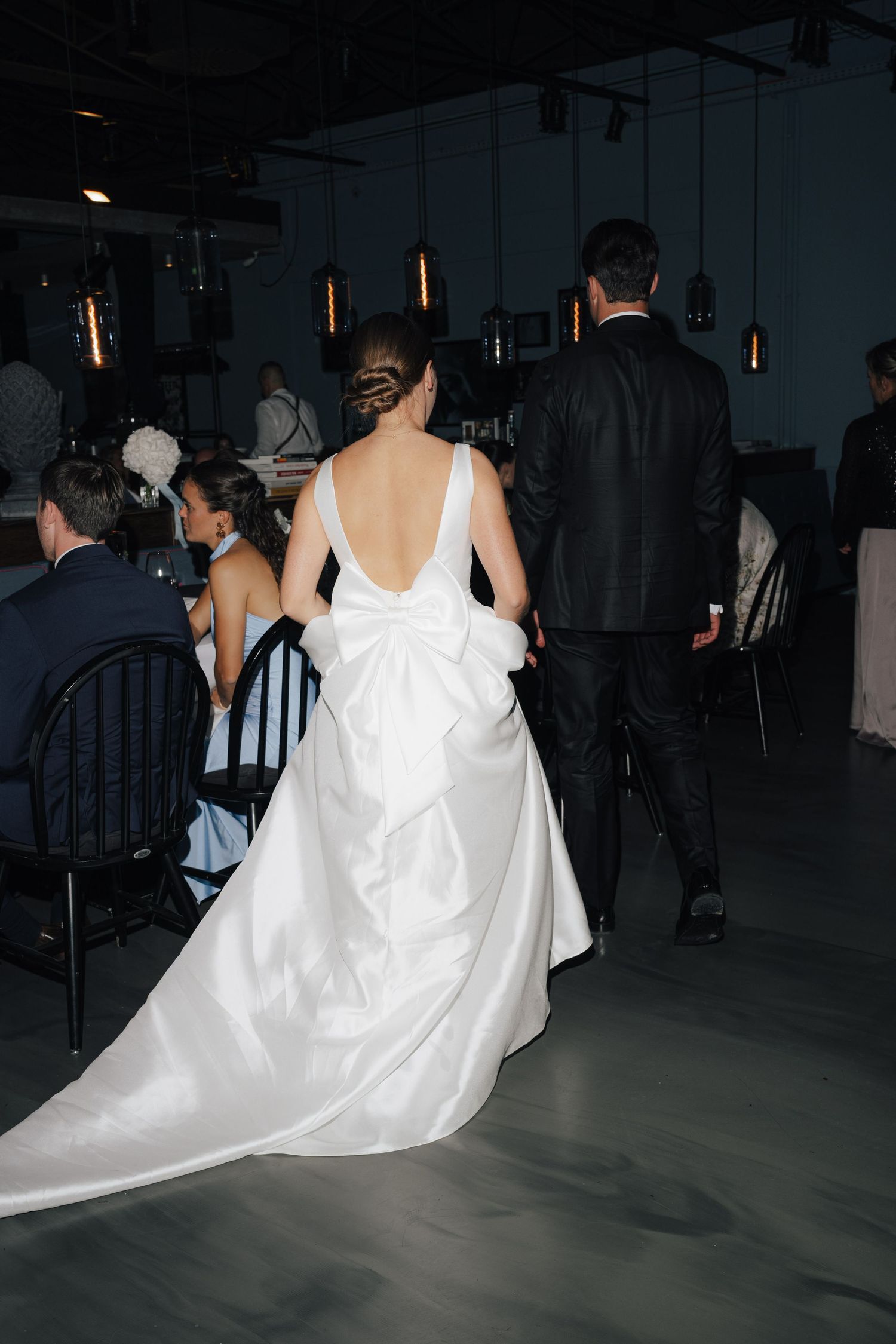 Back view of a flowing white wedding dress with dramatic train at an indoor reception venue.