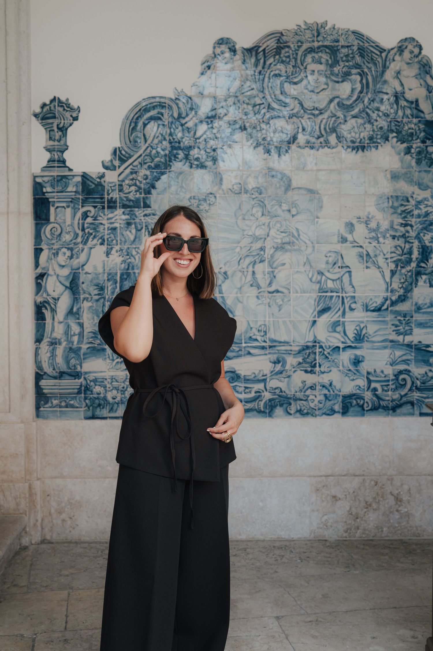 Woman in black dress poses against blue and white tiled wall mural.