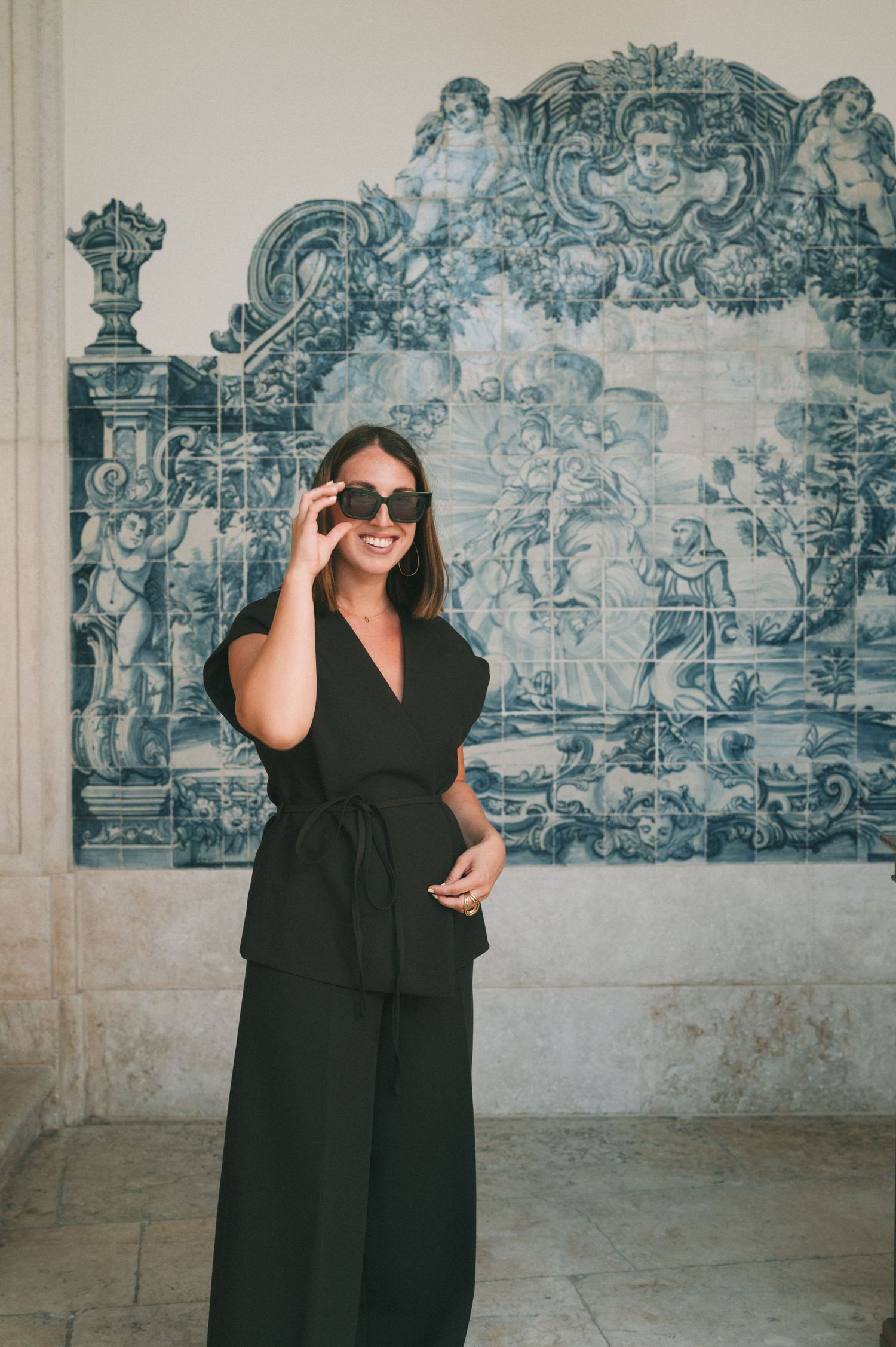 Woman in black dress poses against decorative blue and white tile wall in Portugal.