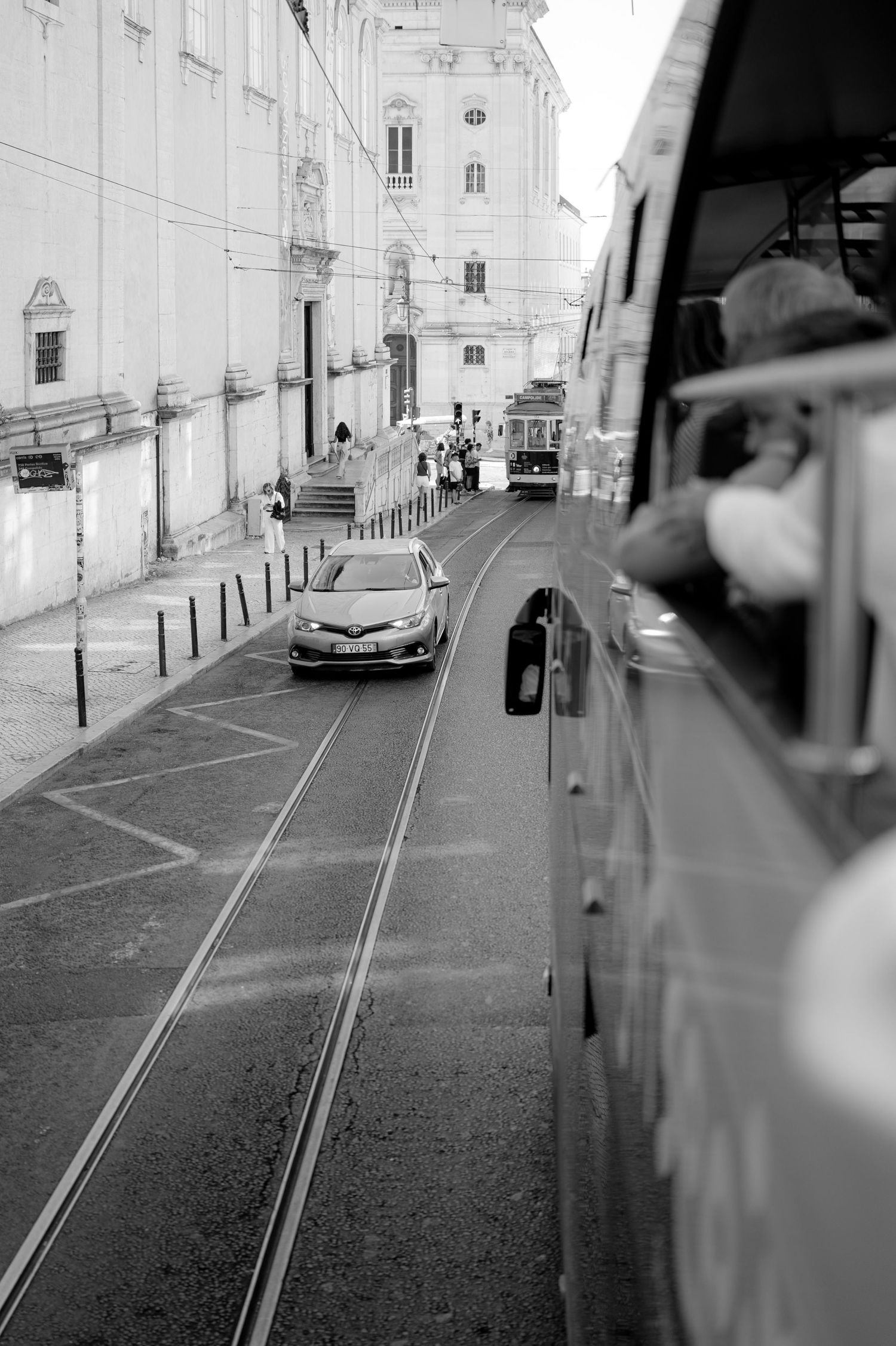 Black and white street scene showing tram tracks through historic Lisbon neighborhood.