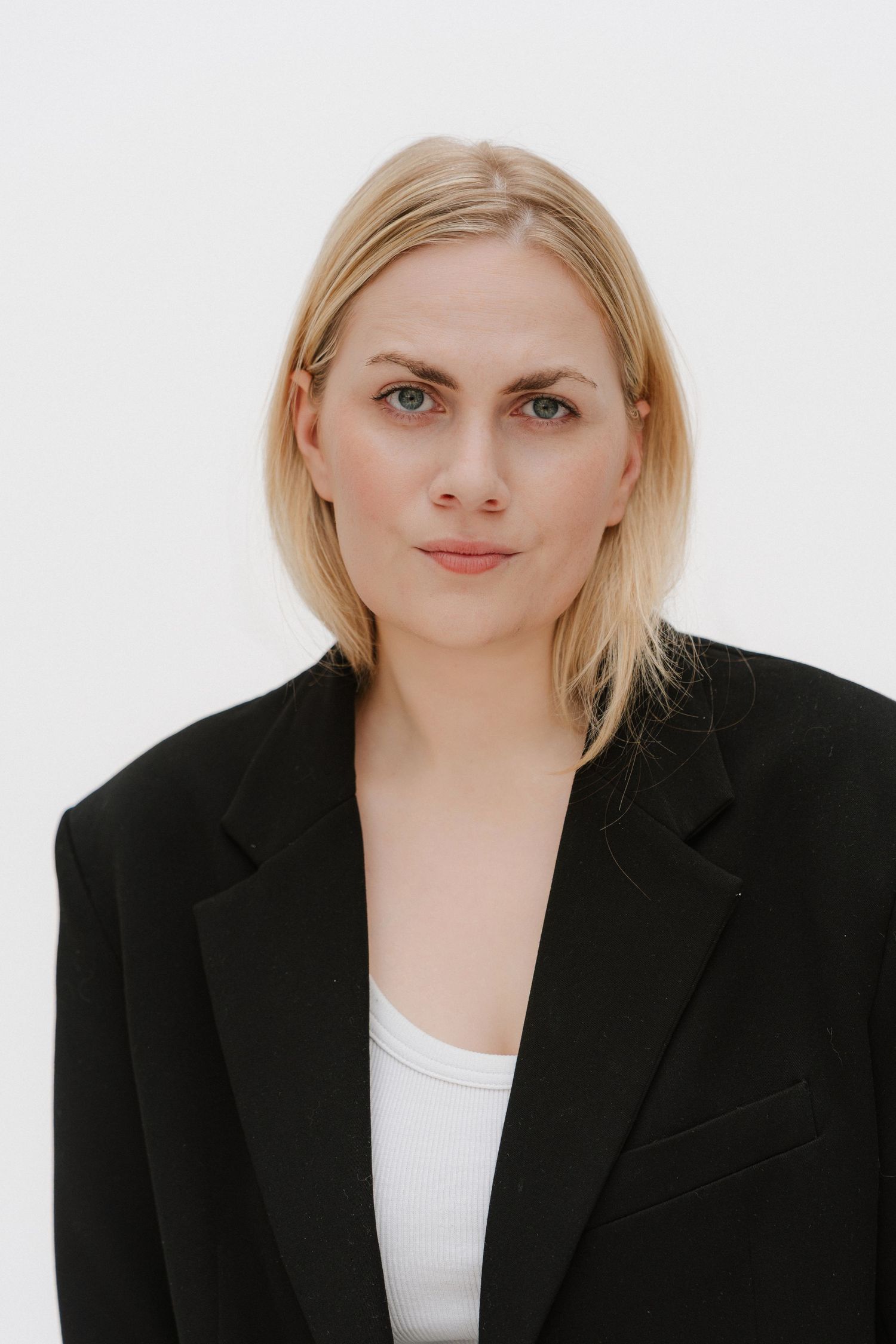 Blonde woman in black blazer and white top poses against white background for professional headshot.