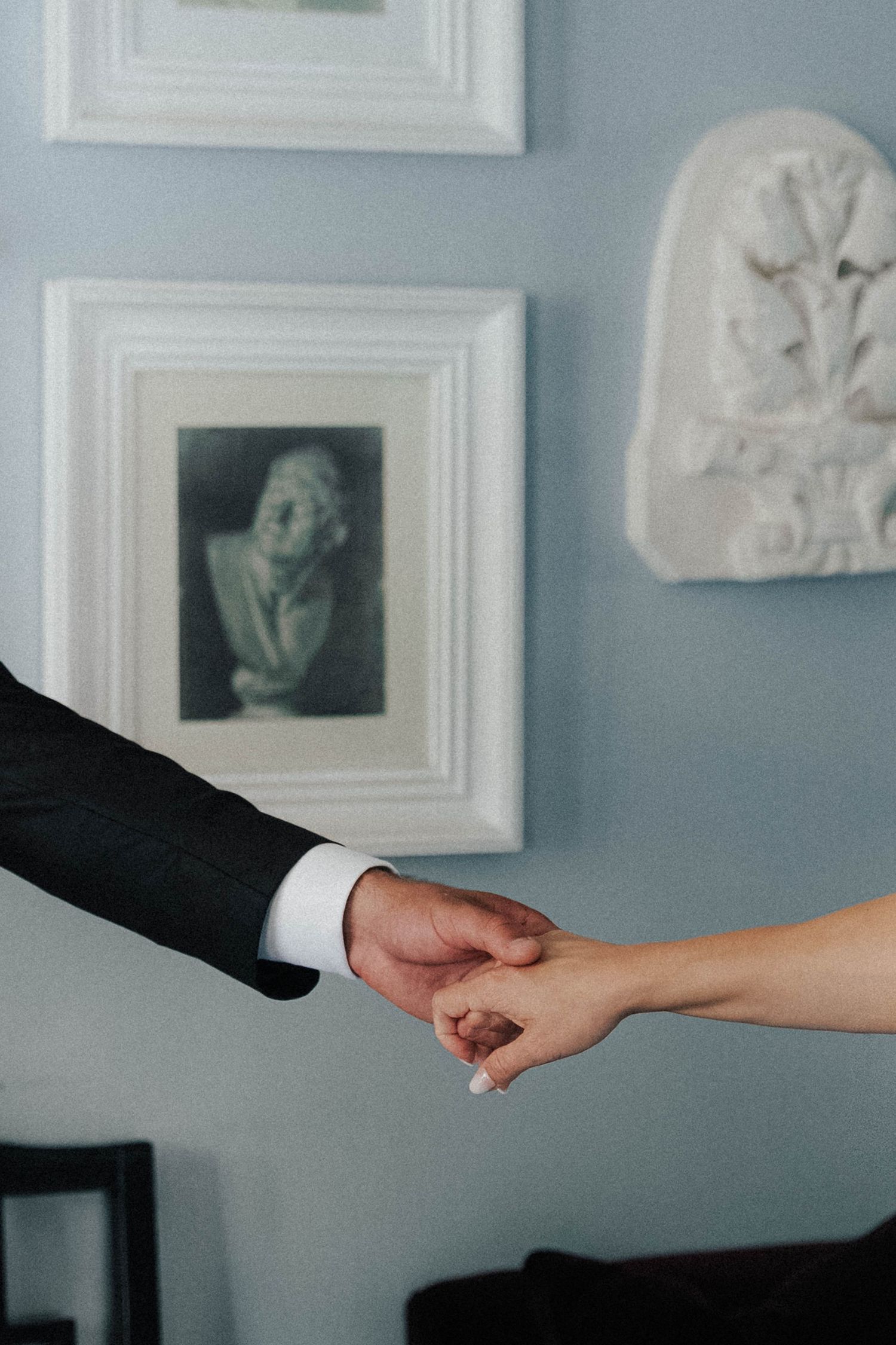 Close-up of hands exchanging papers against a blue wall with framed artwork.