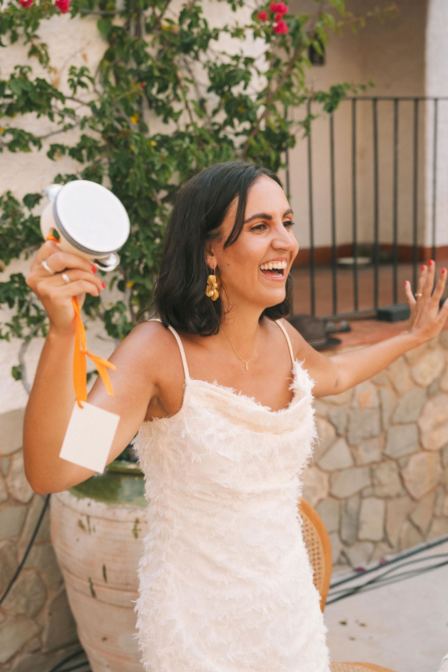 Person in white dress dancing joyfully against stone wall with red flowers.