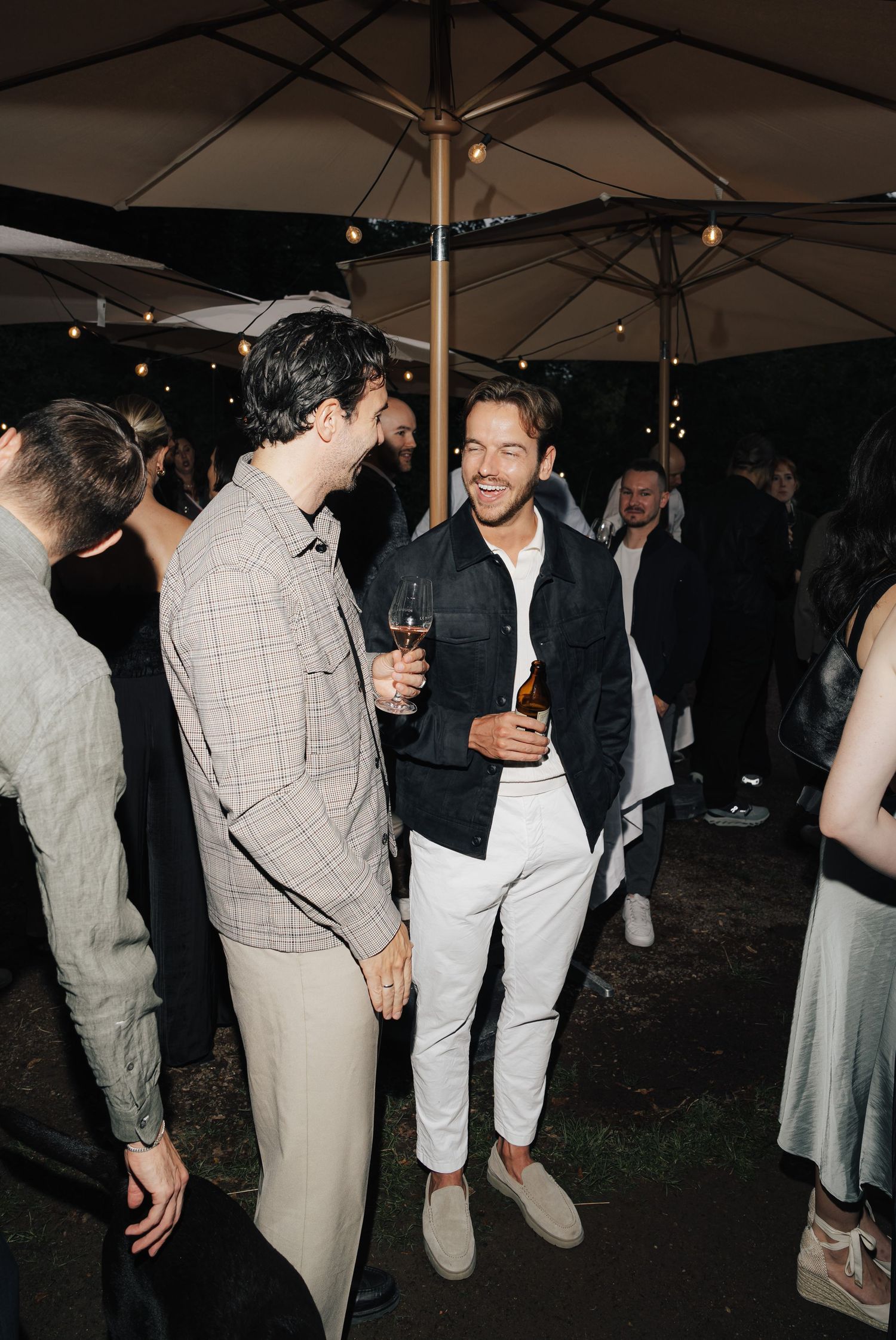 Wedding reception party under outdoor tent with guests mingling and dancing at night.