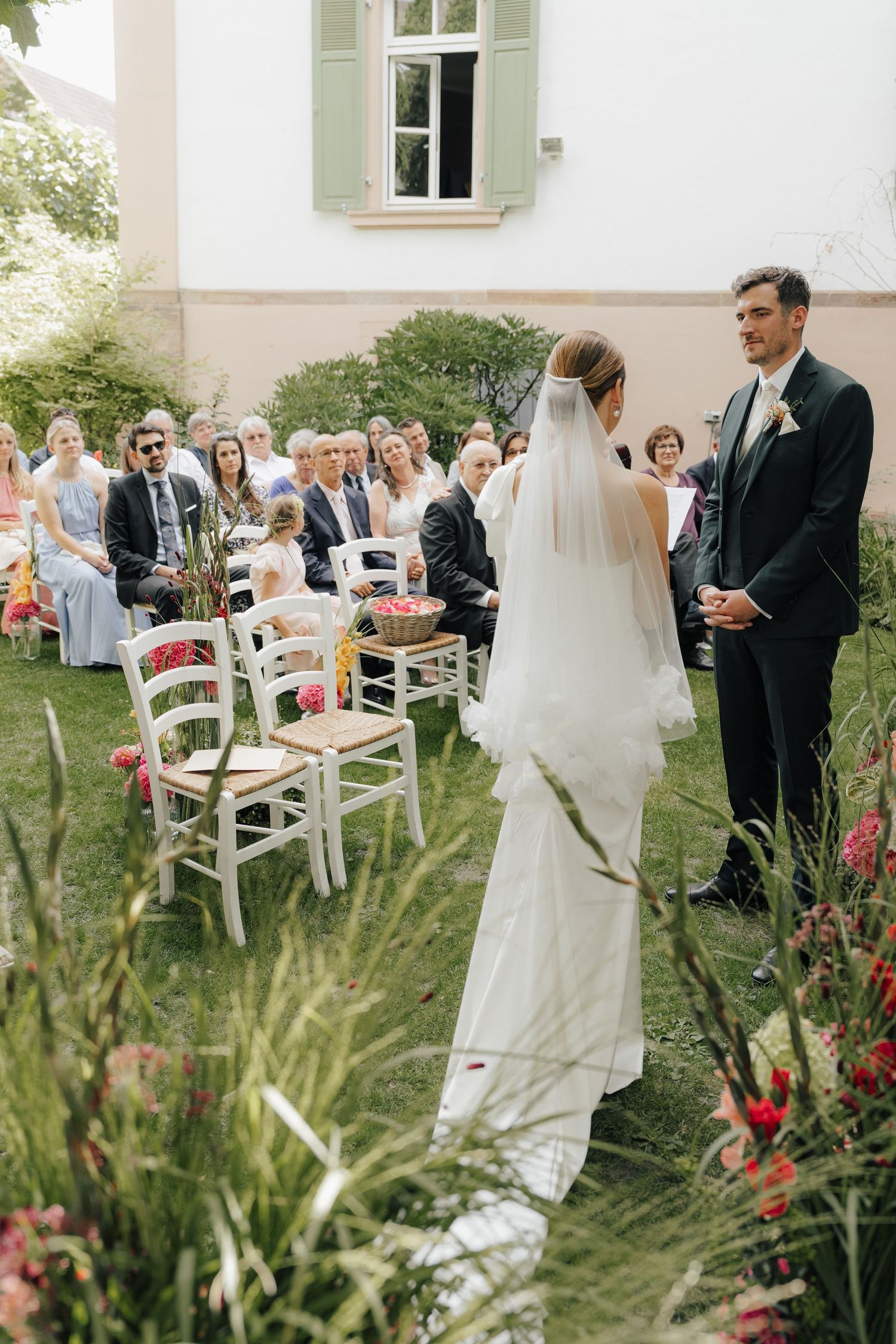 An intimate outdoor garden wedding ceremony with white chairs and colorful wildflowers along the aisle.
