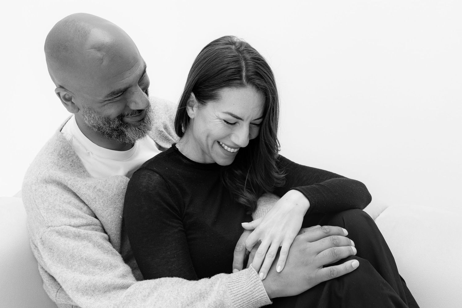 Black and white photo of a smiling couple embracing, woman laughing joyfully as man holds her close.