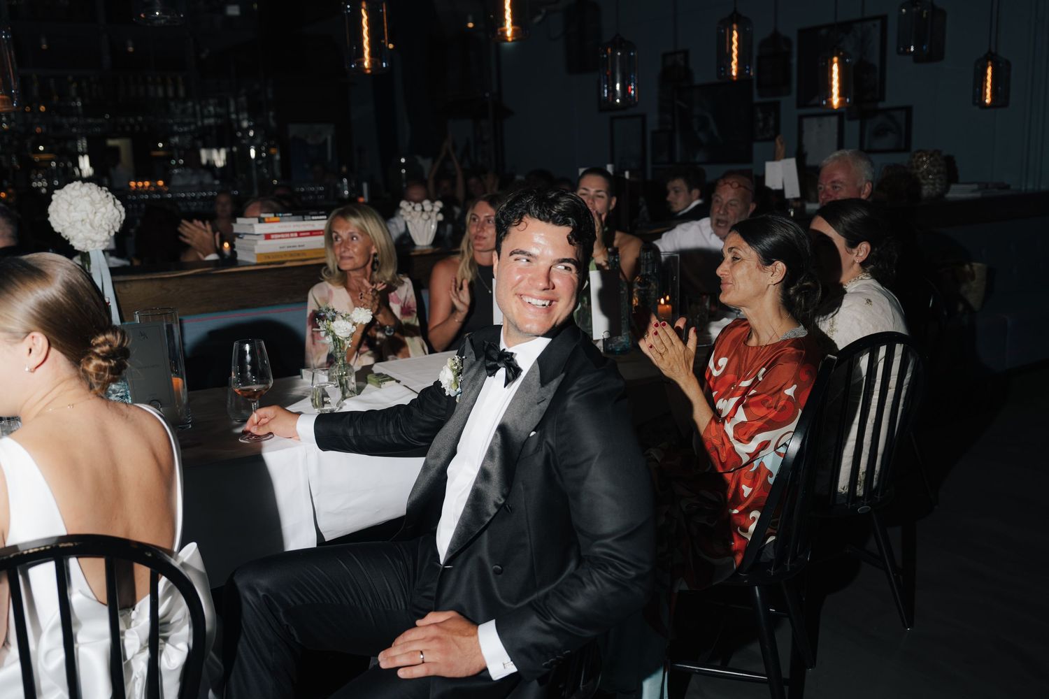 Wedding reception guests enjoying dinner and conversation in formal attire at an intimate venue.