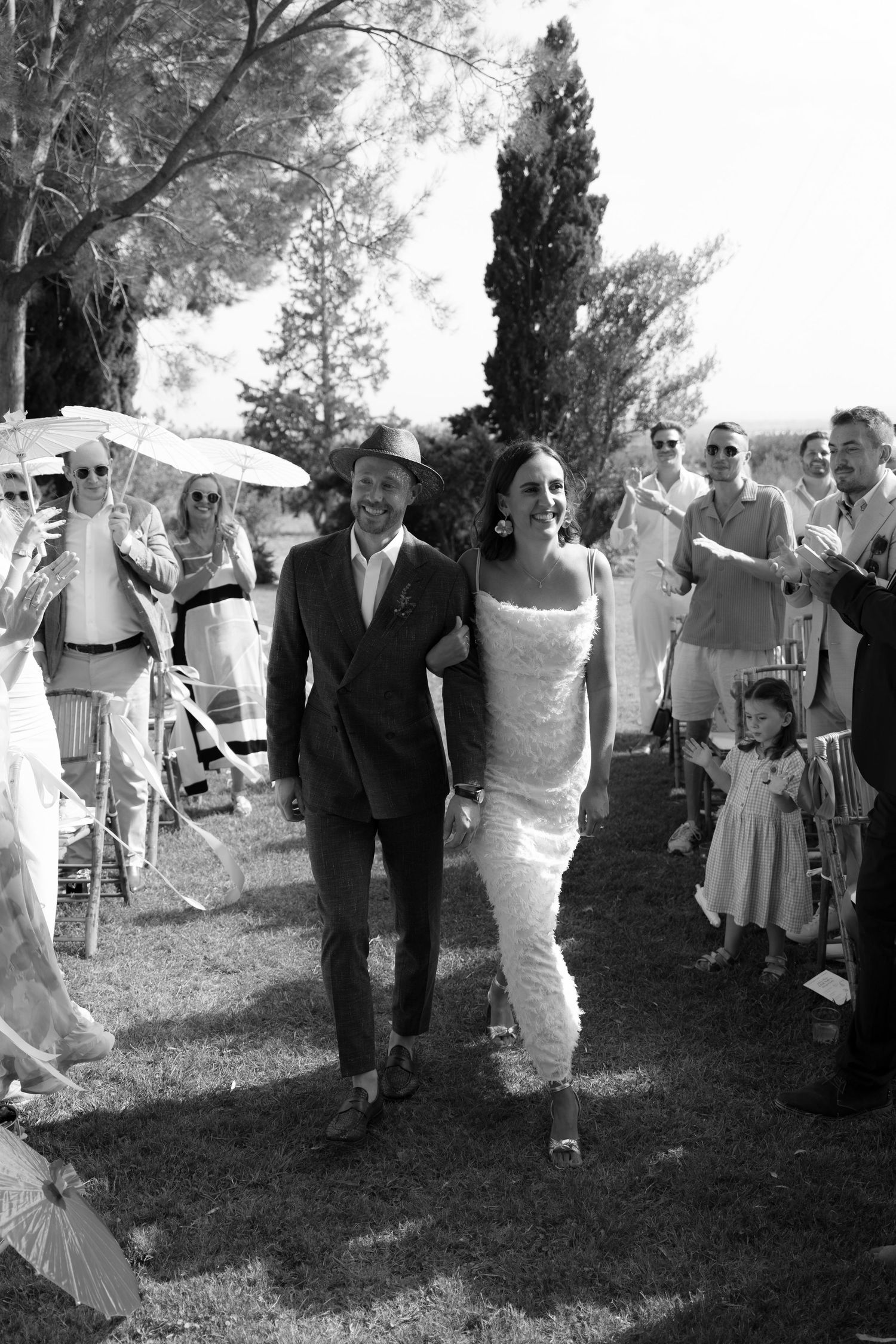 Black and white photo of wedding party walking across grass during outdoor celebration.
