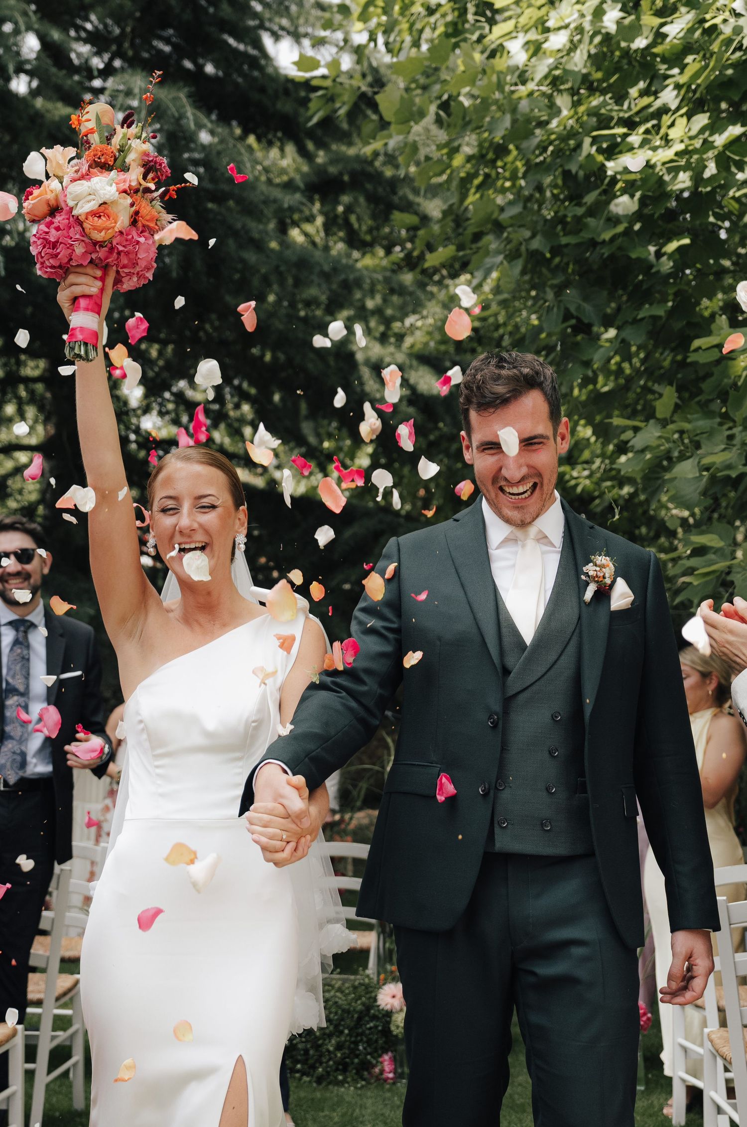 Newlyweds celebrate with flower petals and bouquet toss in a garden wedding setting.