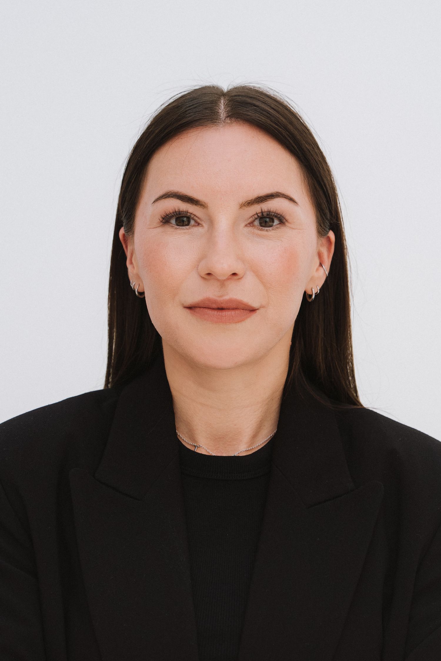 Professional headshot of a woman with dark hair wearing a black blazer against a white background.