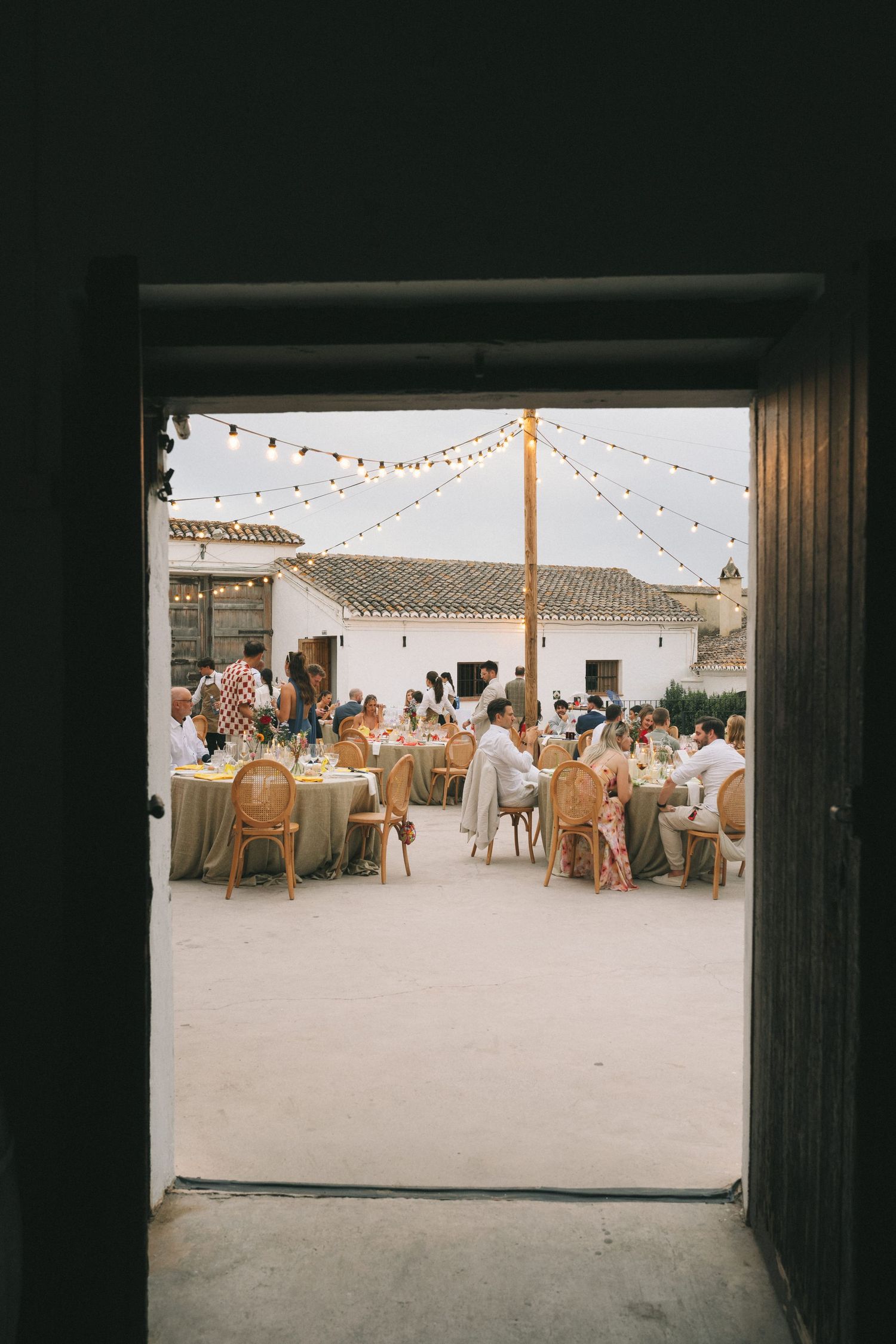Outdoor wedding reception setup with string lights and tables under a white tent canopy.