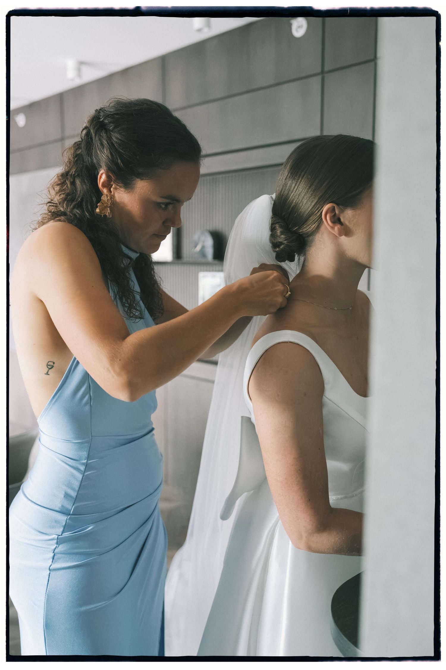 Woman in light blue dress helping with white wedding gown preparations.