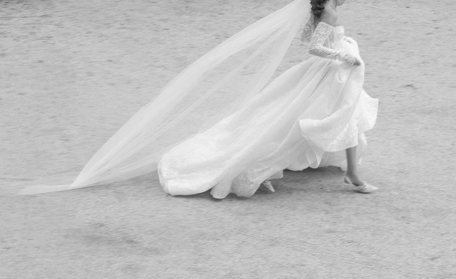 A flowing white wedding dress creates elegant movement across a stone courtyard.