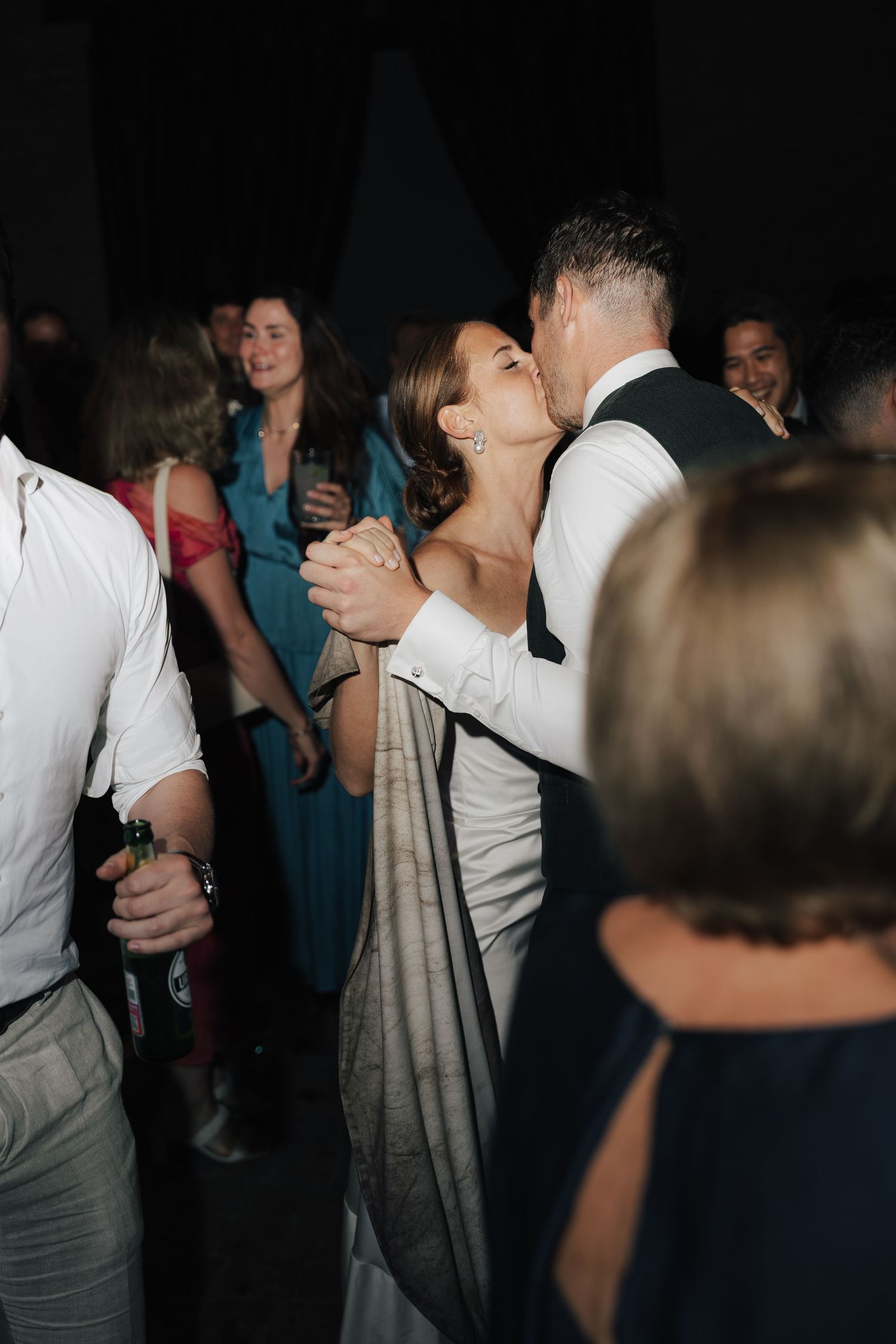 Wedding guests dancing in dimly lit reception venue with formal attire.