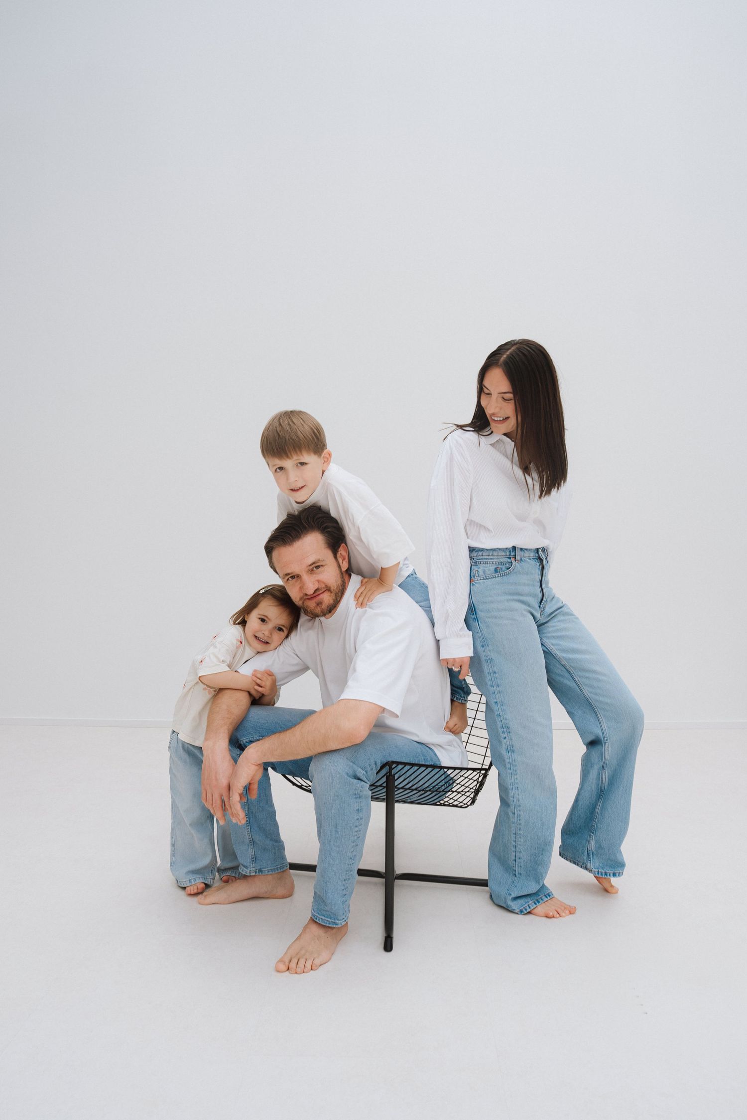Happy family of four in white shirts and jeans posing together on a bench against a white background.
