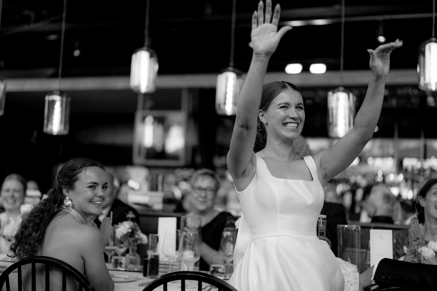 Black and white capture of a celebratory moment at a wedding reception with pendant lights.
