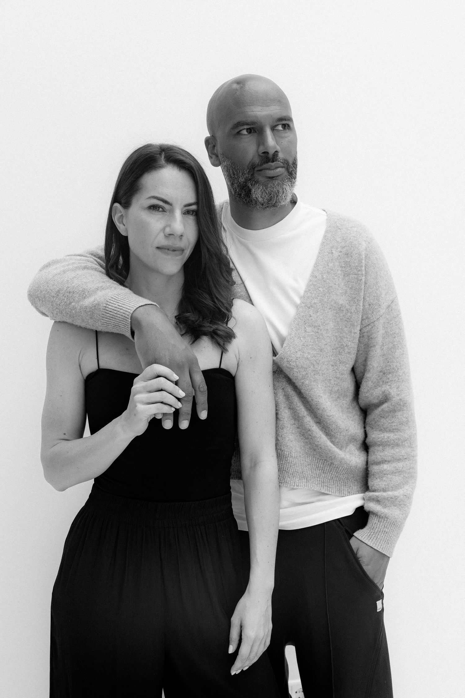 Black and white portrait of a stylish couple posing together against a white background.