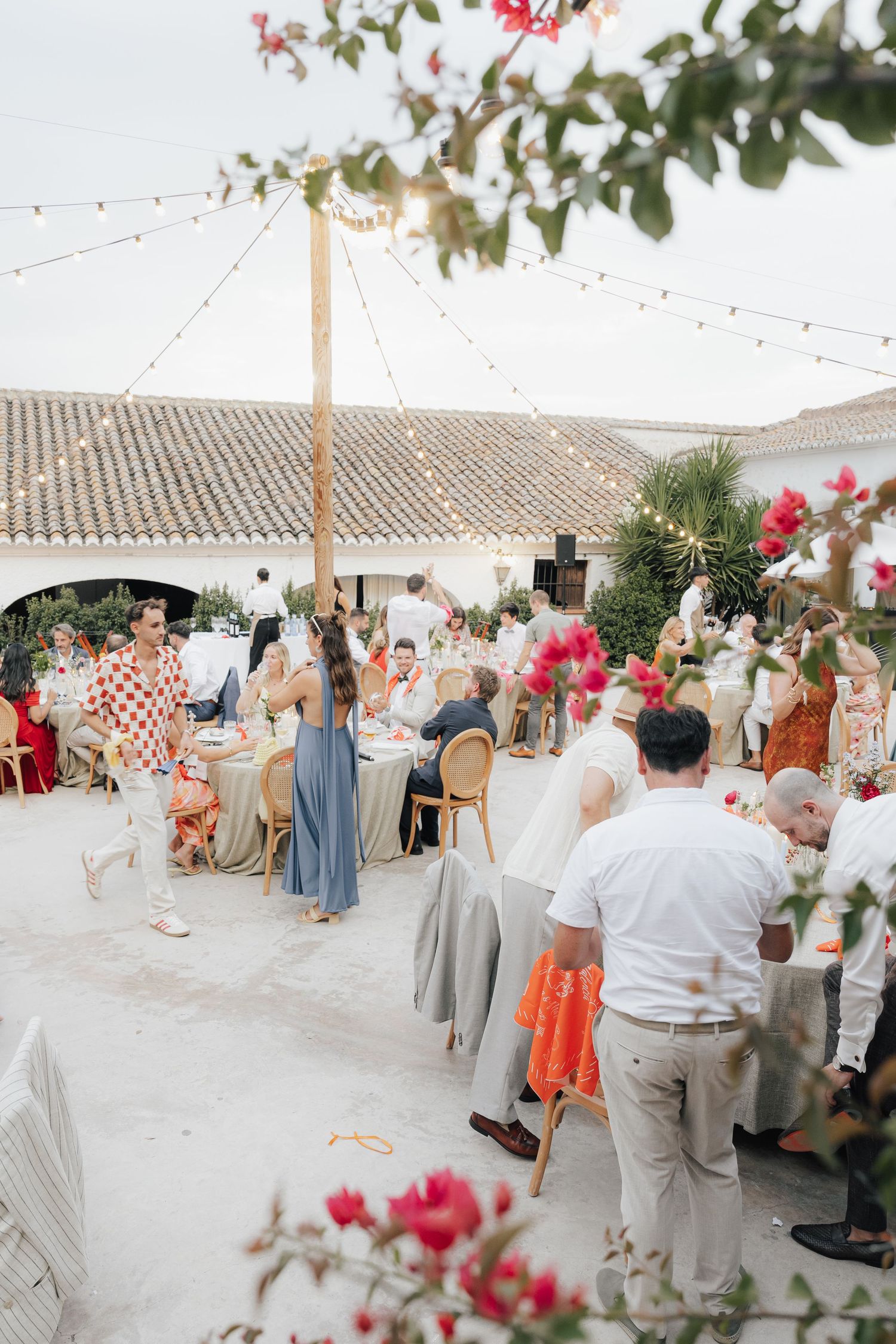Outdoor wedding reception under a white tent with coral floral arrangements and string lights.