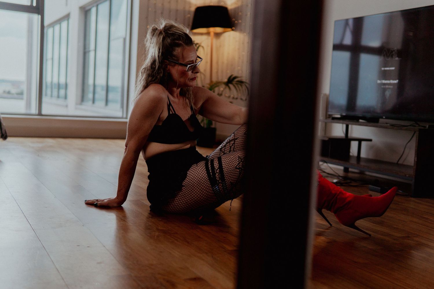 Woman in black lingerie sitting on a wooden floor with red heels nearby. Liverpool boudoir photography