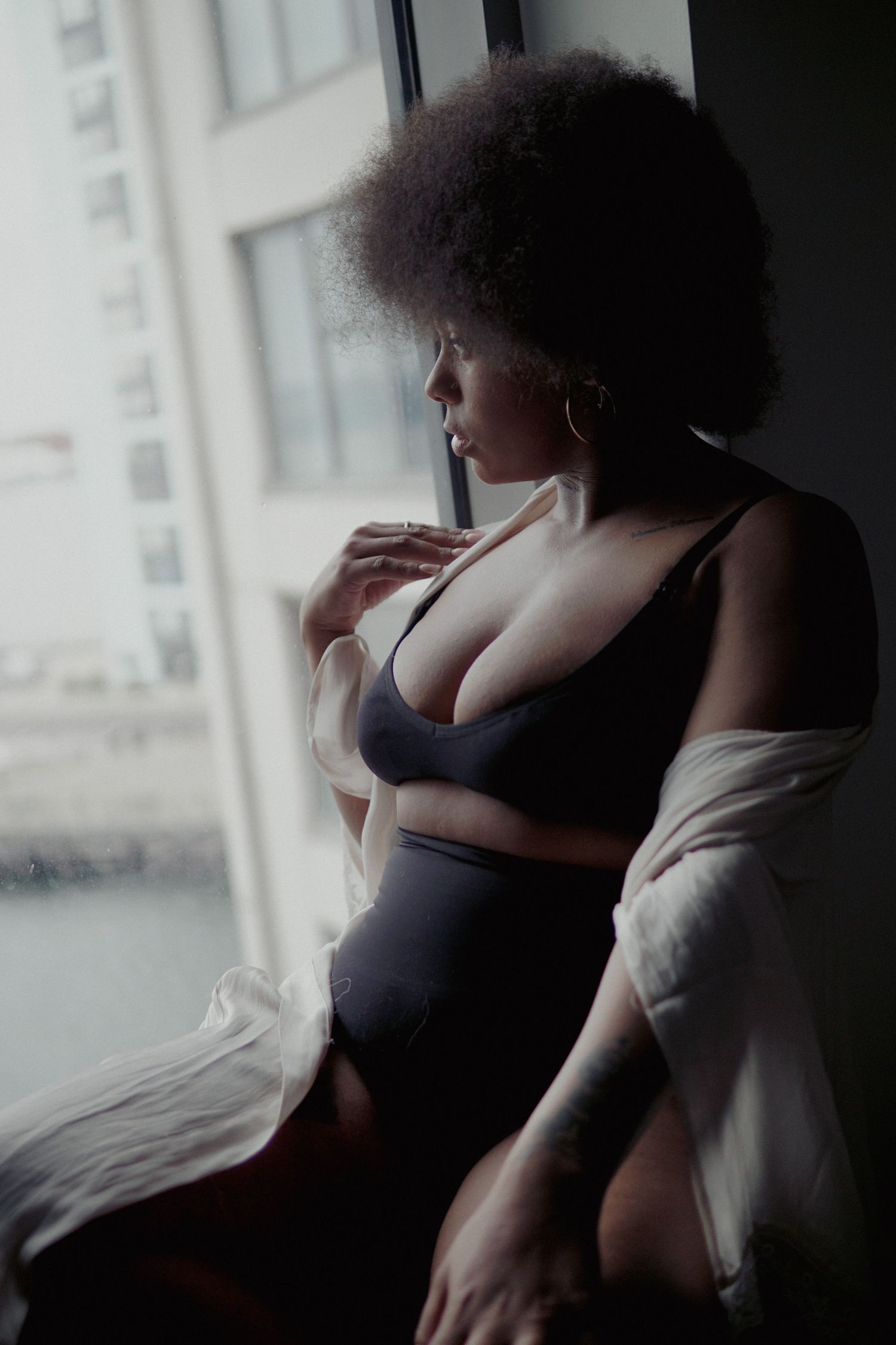 Woman with afro, black underwear set and white silky rob looking in a window Boudoir photography UK Liverpool