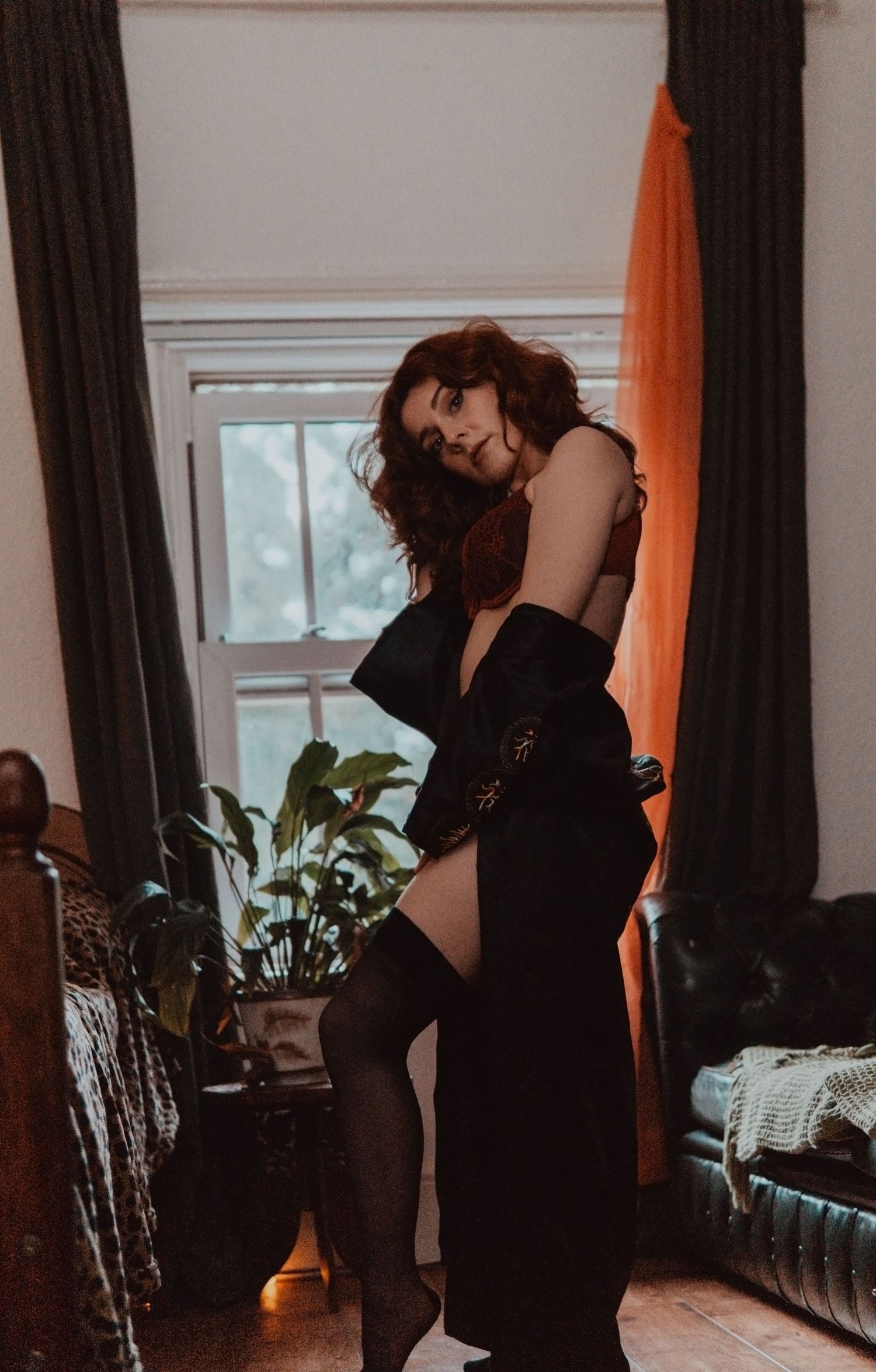Woman with red hair staying in front of the window, wearing red lingerie  Boudoir photography UK Liverpool