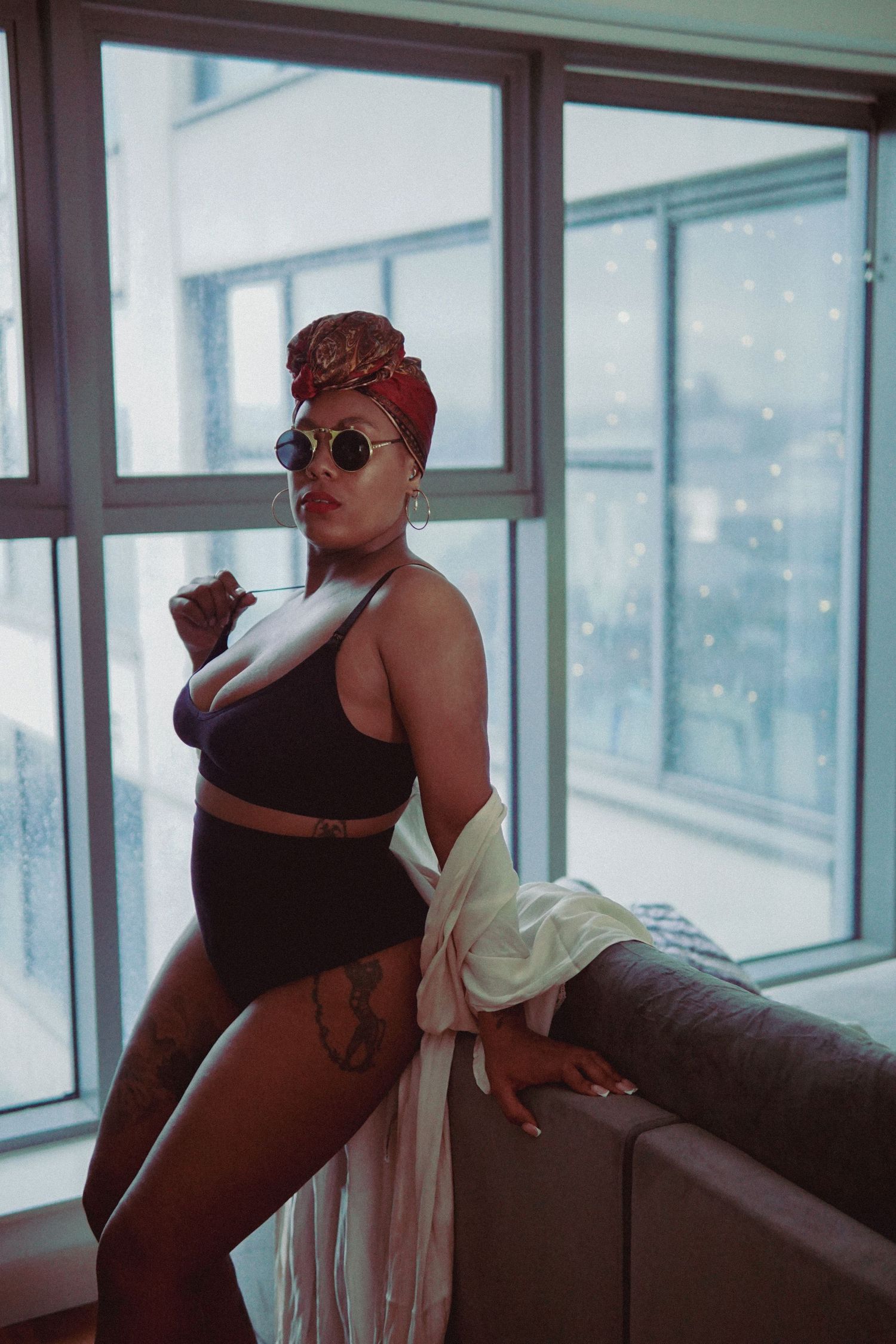 Woman with red headscarf, black matching underwear set and tiny round glasses posing on a edge of sofa Boudoir photography UK Liverpool