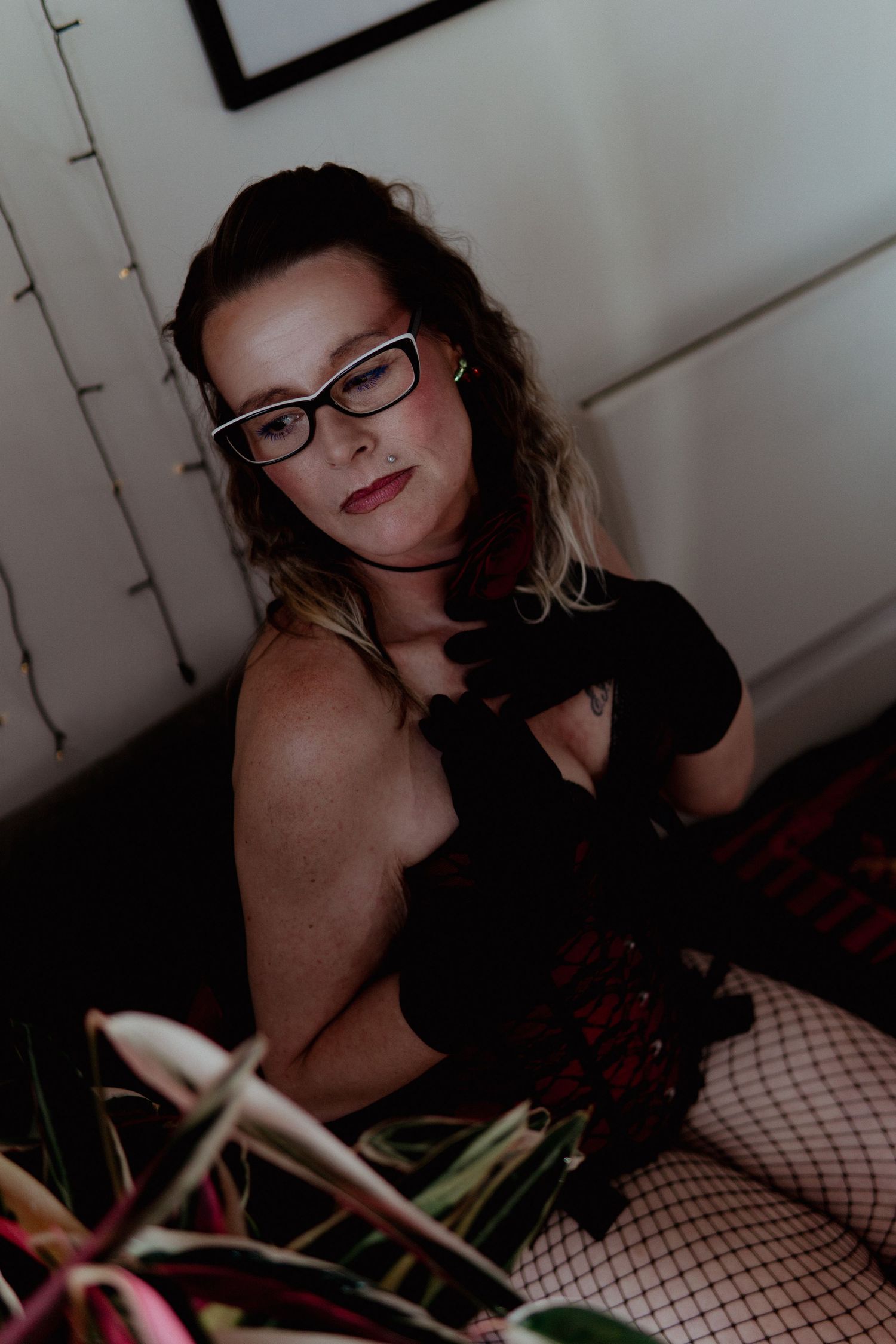 Woman in black lingerie and glasses sitting among houseplants. Liverpool boudoir photography