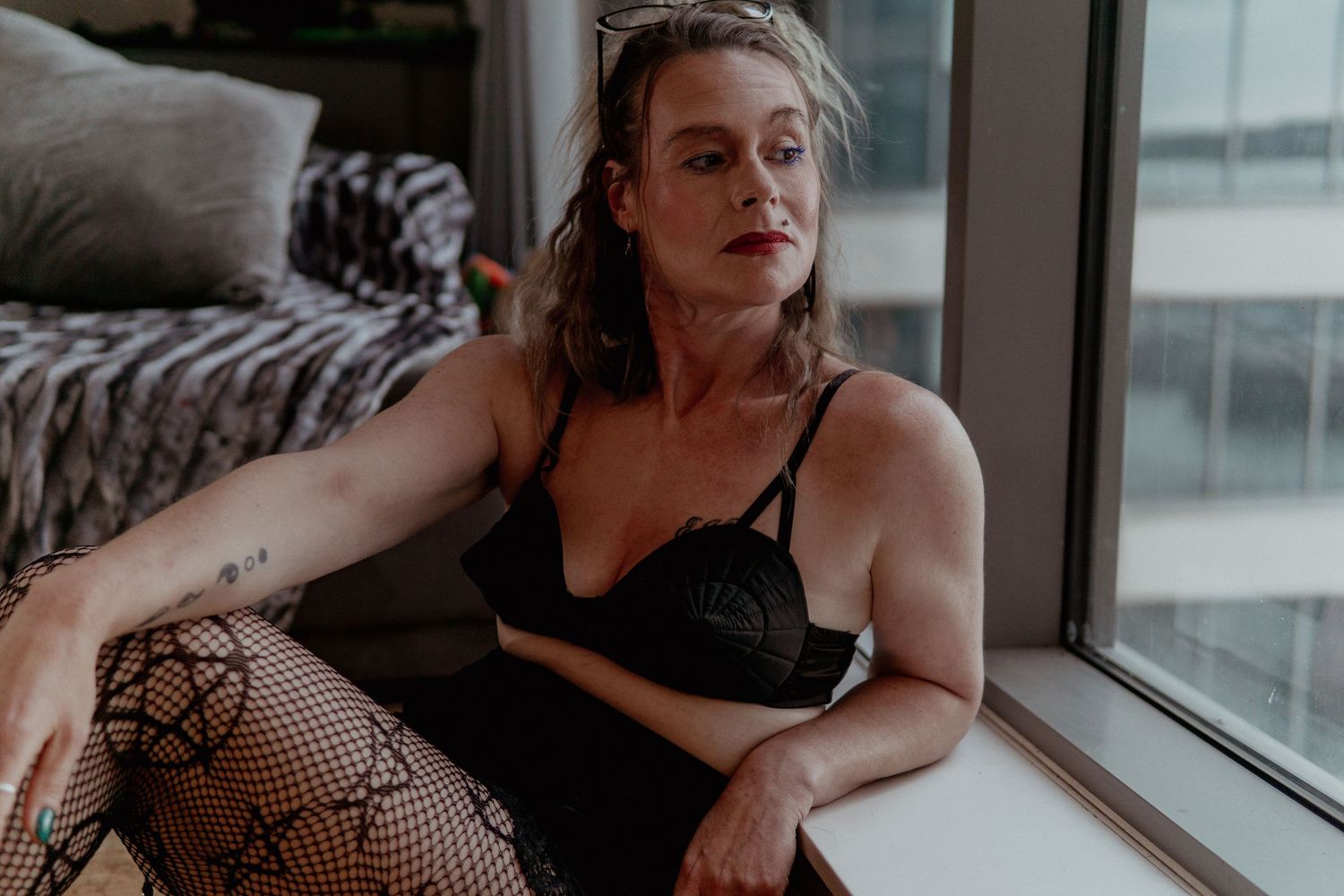 Woman in black bra and fishnet stockings sitting by a window. Liverpool boudoir photography