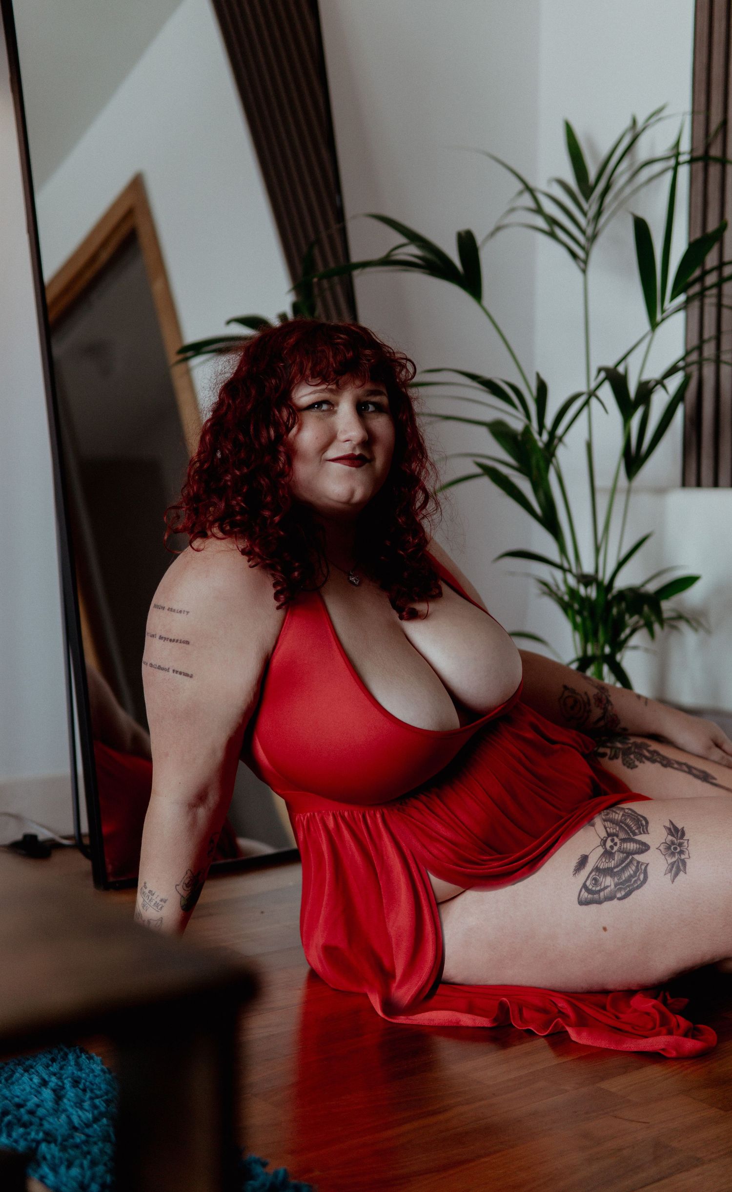 Woman in red dress and tattoos  sitting on a floor Boudoir photography UK Liverpool