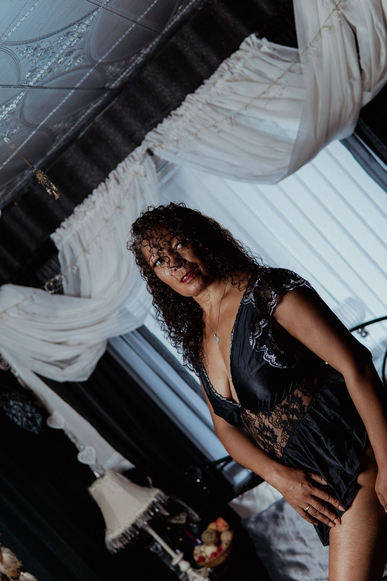 Woman in black satin lace teddy with curly hair posing in ornate boudoir setting. Liverpool boudoir photography