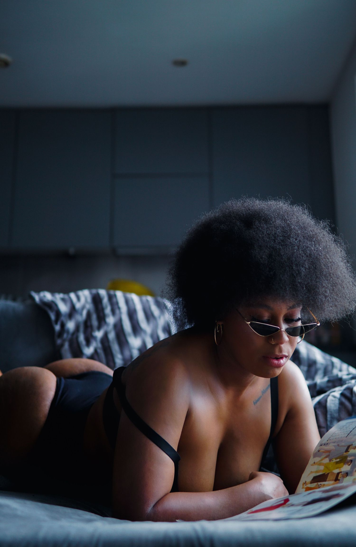 Woman with afro, tiny sunglasses laying on her stomach and reading magazine Boudoir photography UK Liverpool